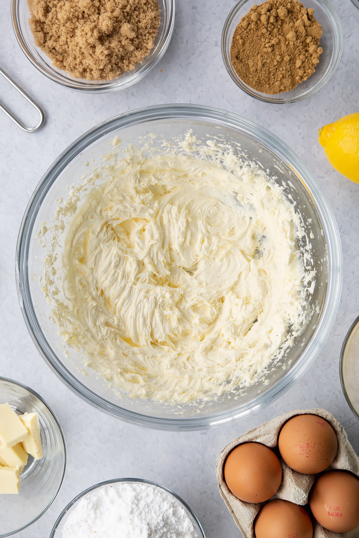 Buttercream in a glass mixing bowl. Ingredients to make Gingerbread Swiss roll surround the bowl.