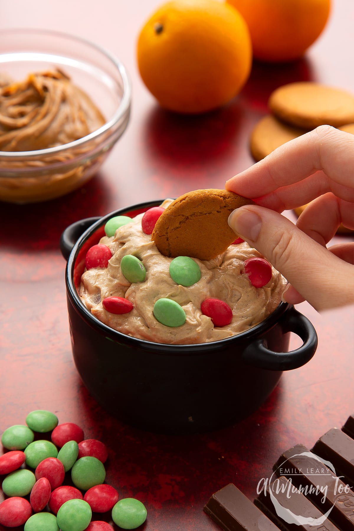Christmas cookie dip in a black pot. A hand dips a piece of gingernut cookie out of the dip.