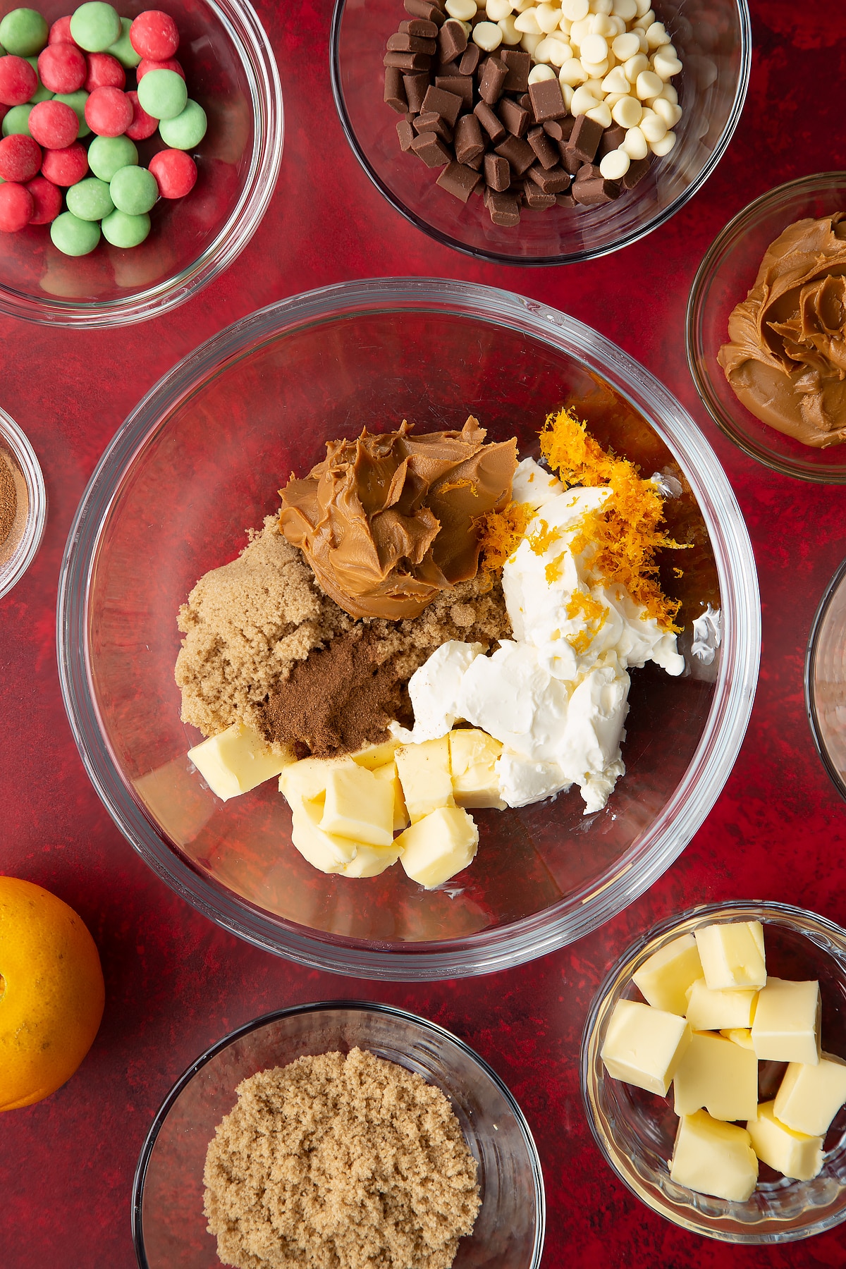 Butter, cream cheese, Biscoff spread, sugar, orange zest and cinnamon in a mixing bowl. Ingredients to make Christmas cookie dip surround the bowl.