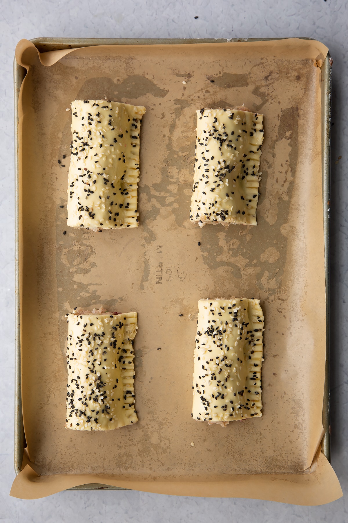 Four raw festive sausage rolls on a baking tray lined with baking paper.