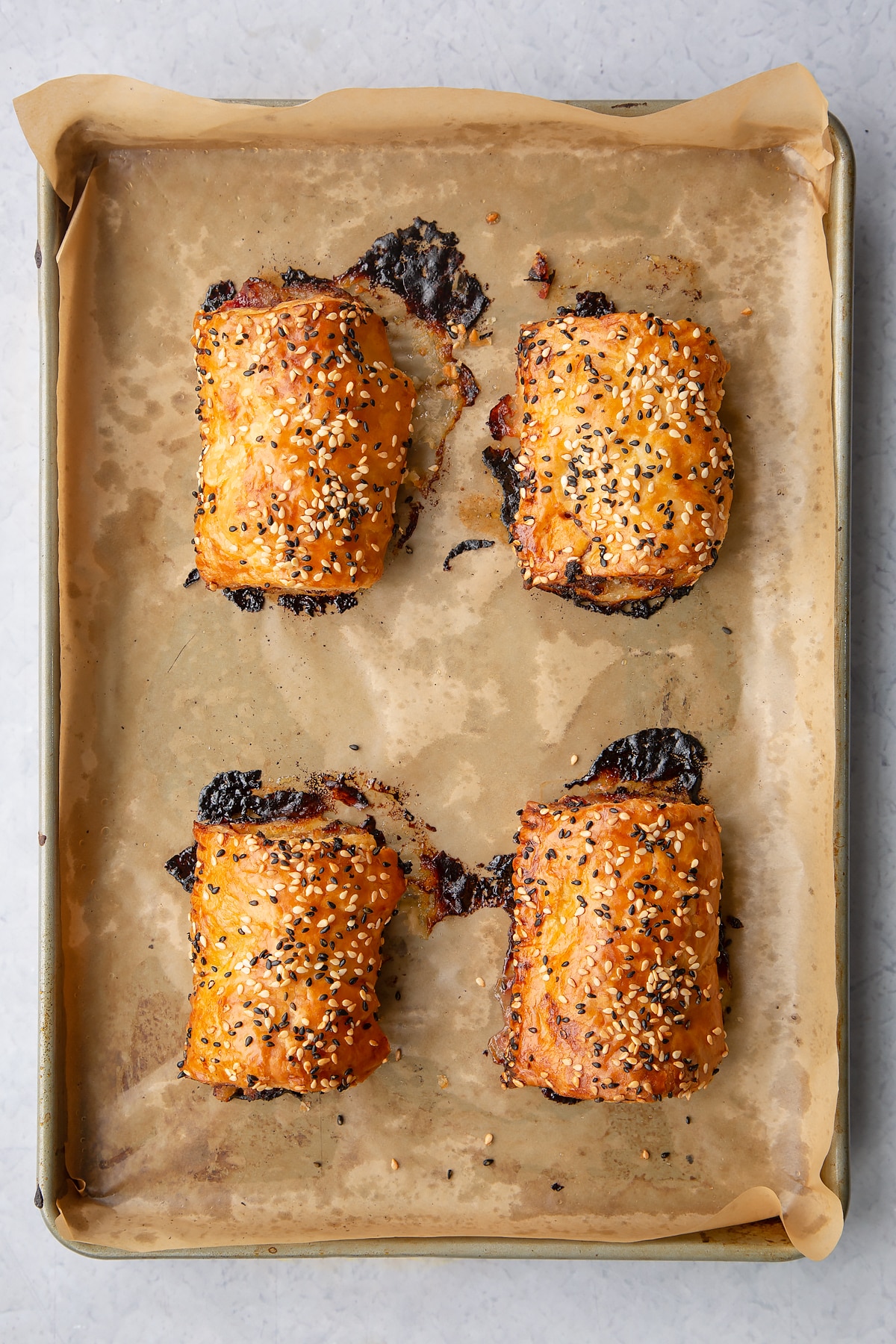 Four freshly baked festive sausage rolls on a baking tray lined with baking paper.