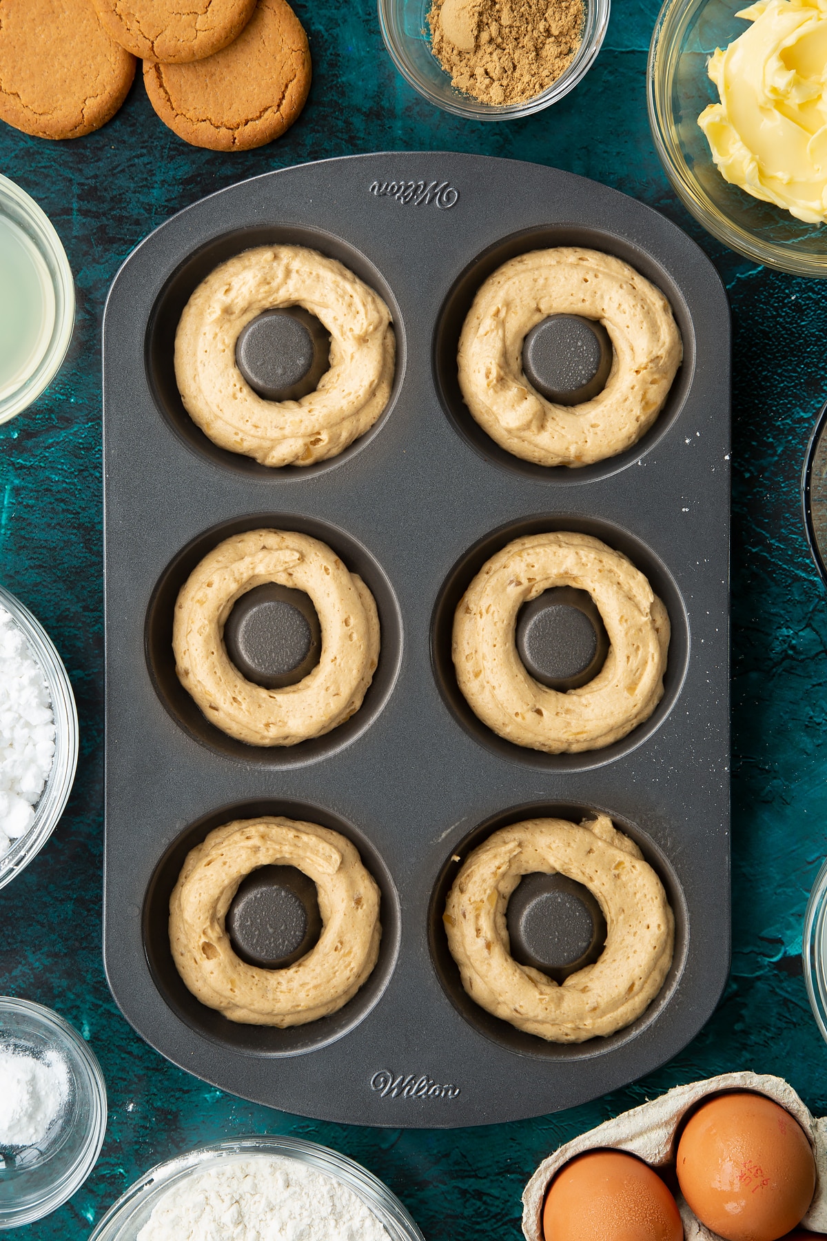 A metal donut pan with gingerbread donut batter piped into it.
