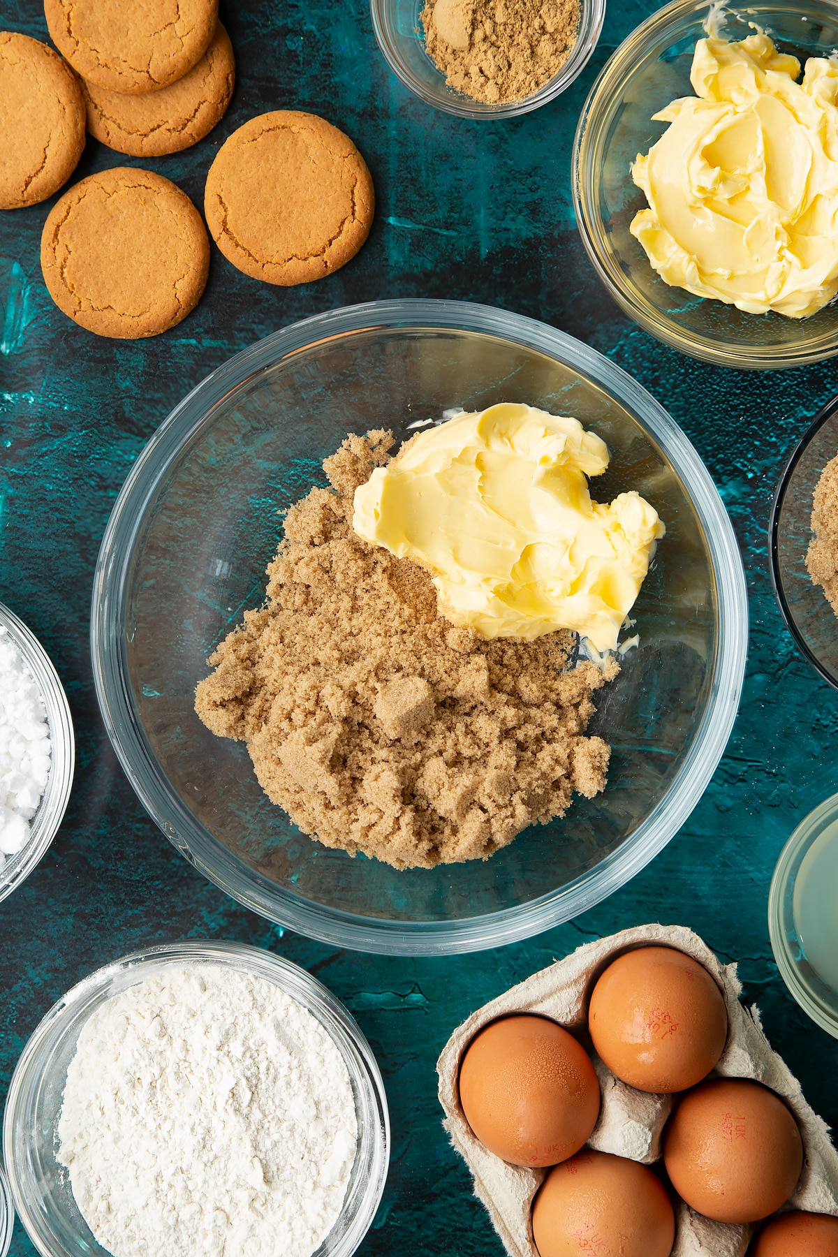 Butter and brown sugar in a glass mixing bowl. Ingredients to make gingerbread donuts surround the bowl.