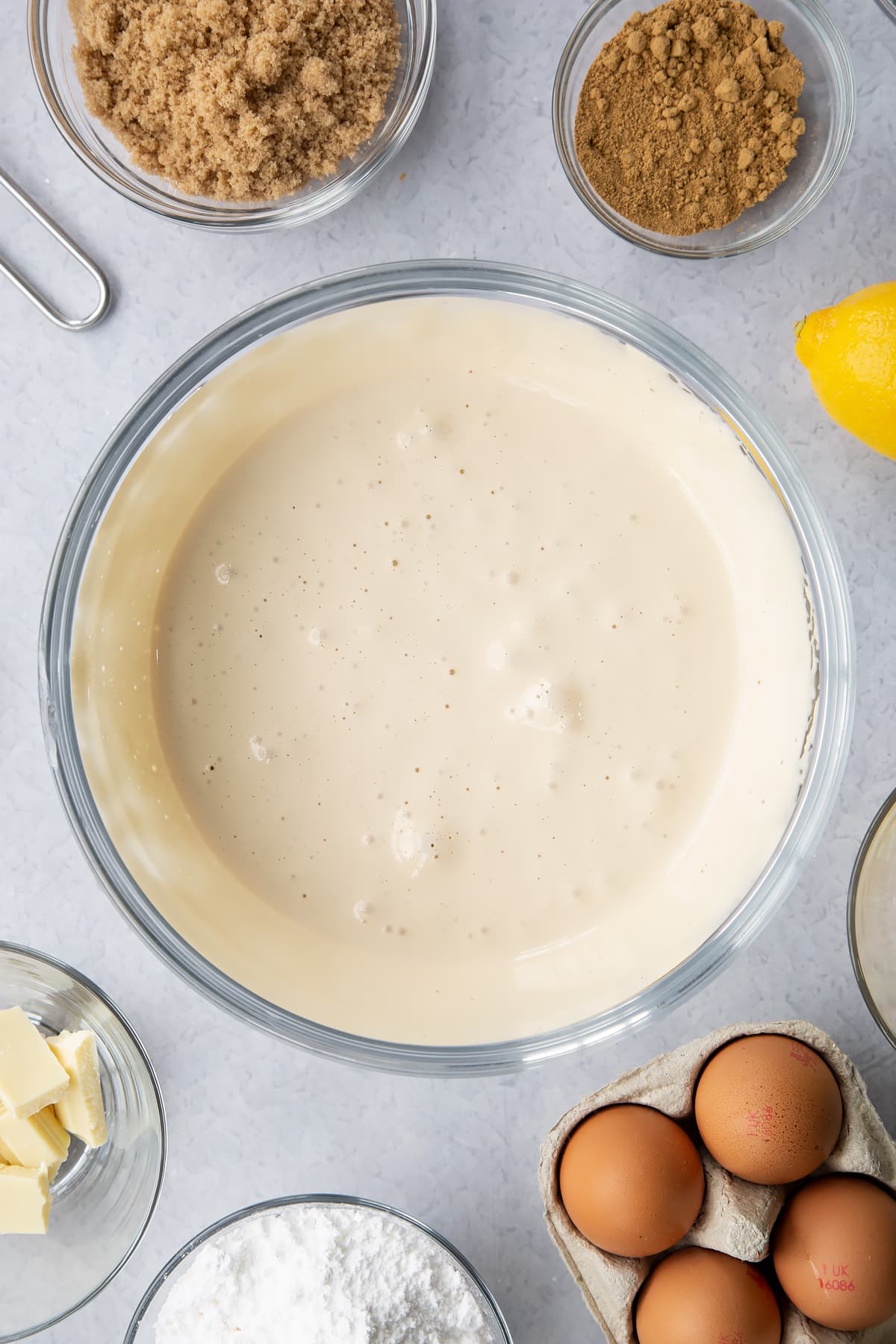 Eggs and light soft brown sugar whisked to a pale, thick mixture in a glass mixing bowl. Ingredients to make Gingerbread Swiss roll surround the bowl.