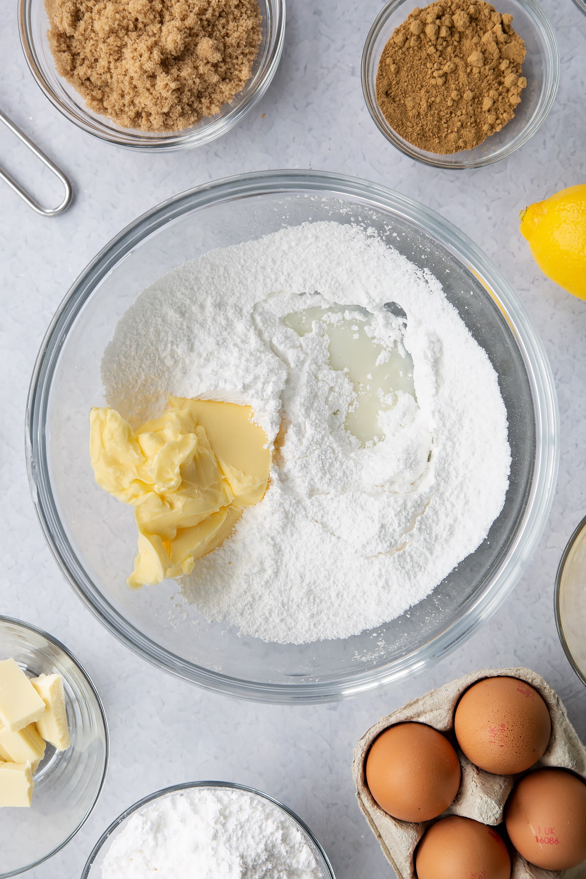 Icing sugar, butter and milk in a glass mixing bowl. Ingredients to make Gingerbread Swiss roll surround the bowl.