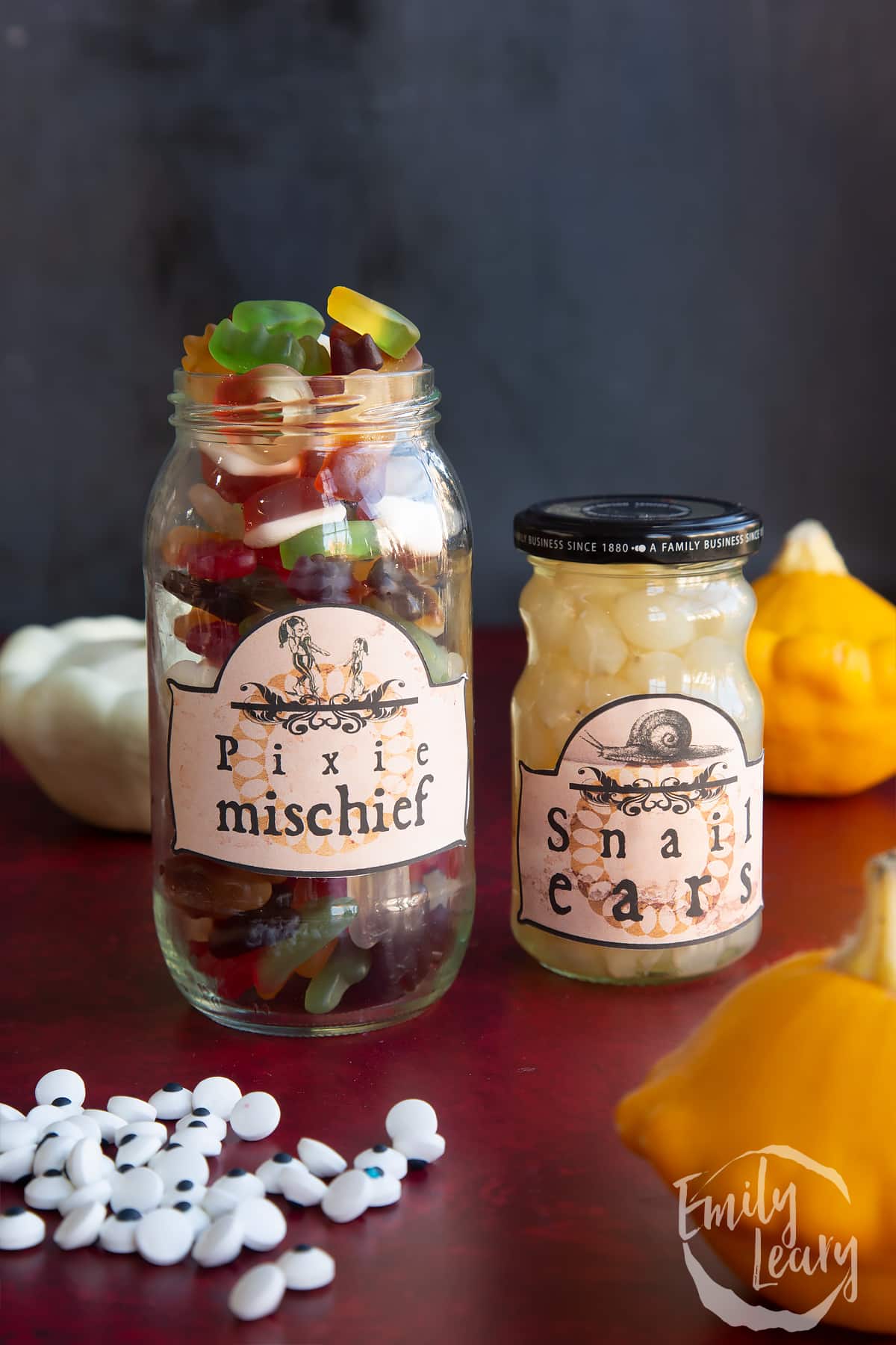 Two jars of different sizes, bearing Halloween apothecary labels. The jars contain mini gummy sweets (Pixie mischief) and baby pickled onions (Snail ears).