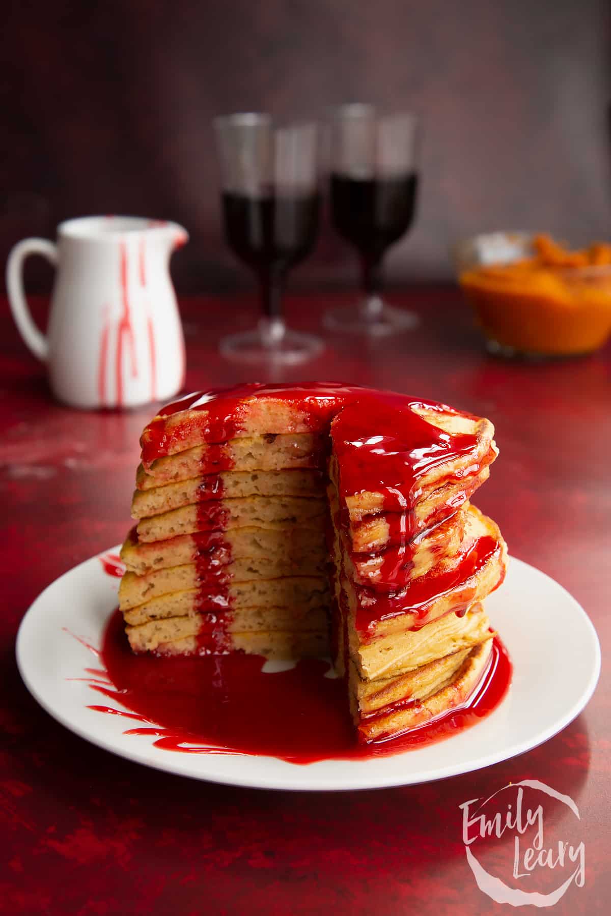 Halloween pancakes stacked on a white plate, drizzled with red syrup. A section has been cut away.