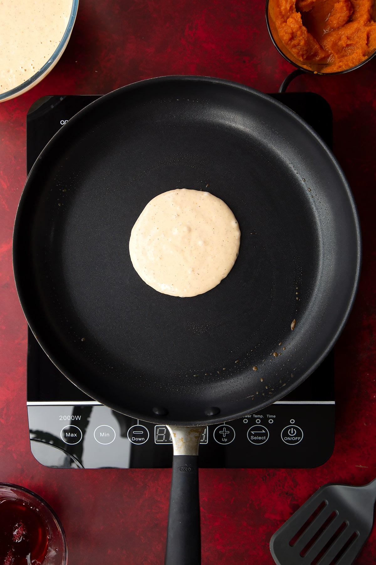 Pumpkin pancake batter in a greased frying pan. Ingredients to make Halloween pancakes surround the pan.