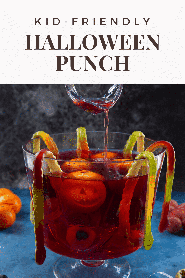 Halloween punch, decorated with fruit and gummy snakes. Some punch is being ladled from the bowl. Caption reads: Kid friendly Halloween punch.