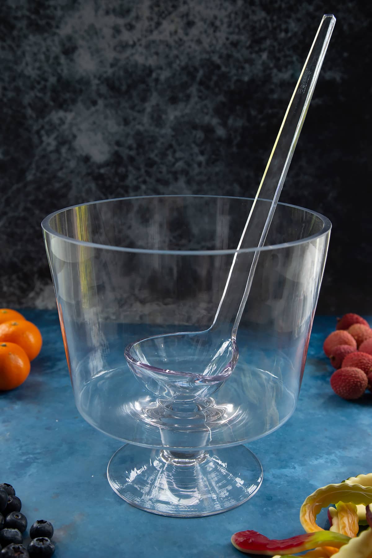 A glass punch bowl with ladle. Ingredients to make Halloween punch surround the bowl.