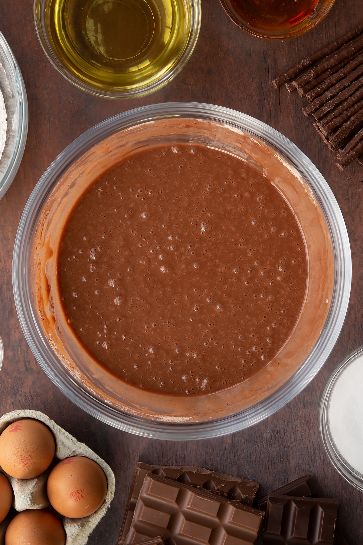 Chocolate cake batter in a glass mixing bowl. Ingredients to make Matchmaker cake surround the bowl.