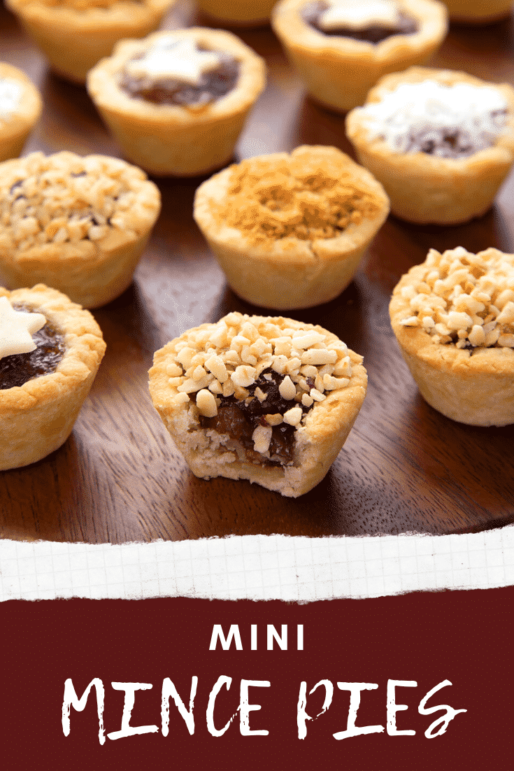 Mini mince pie on a dark wooden board, topped with chopped nuts crumbs with a bite out of it. Caption reads: Mini mince pies.
