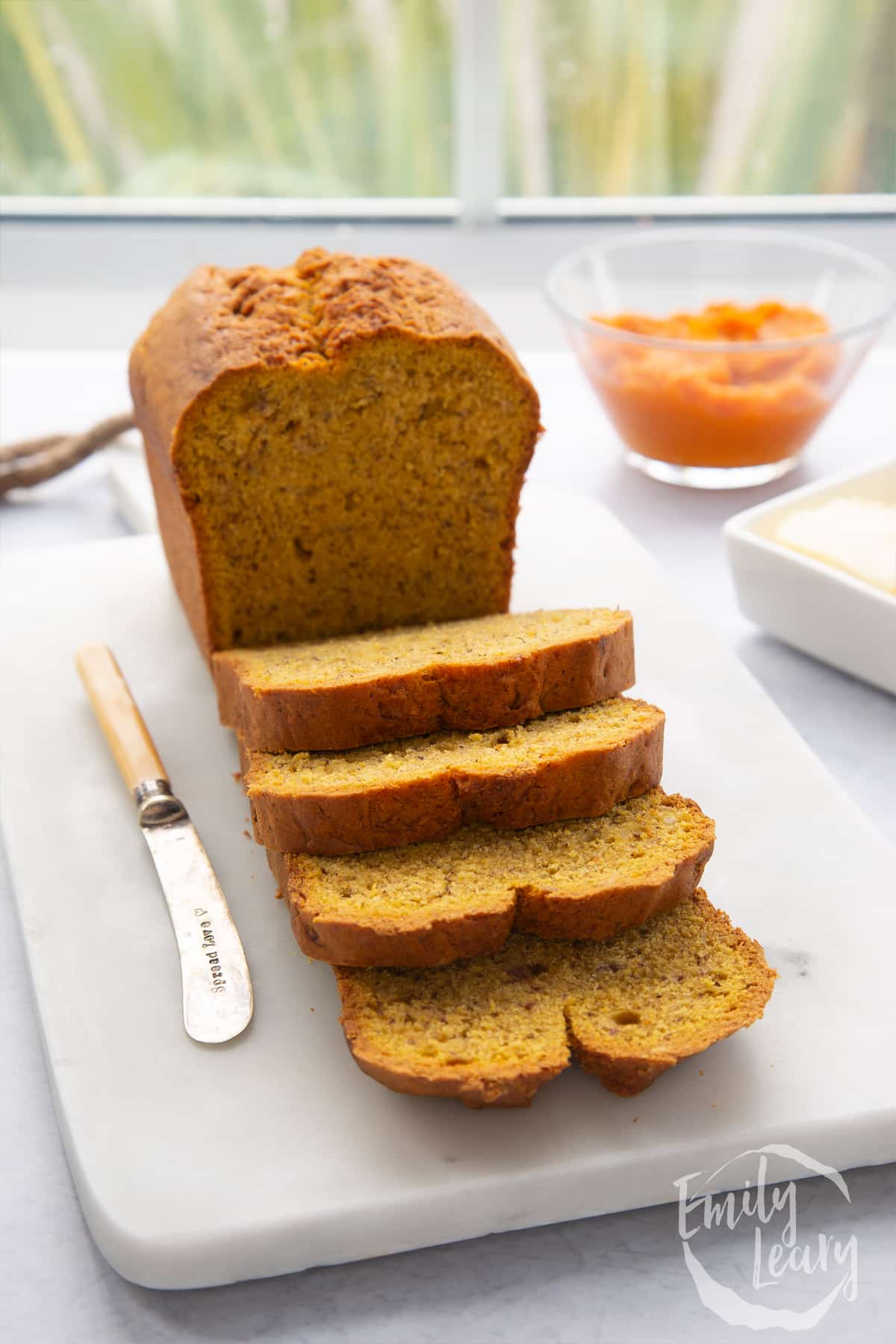 A pumpkin banana bread loaf on a white marble board. Some has been sliced.