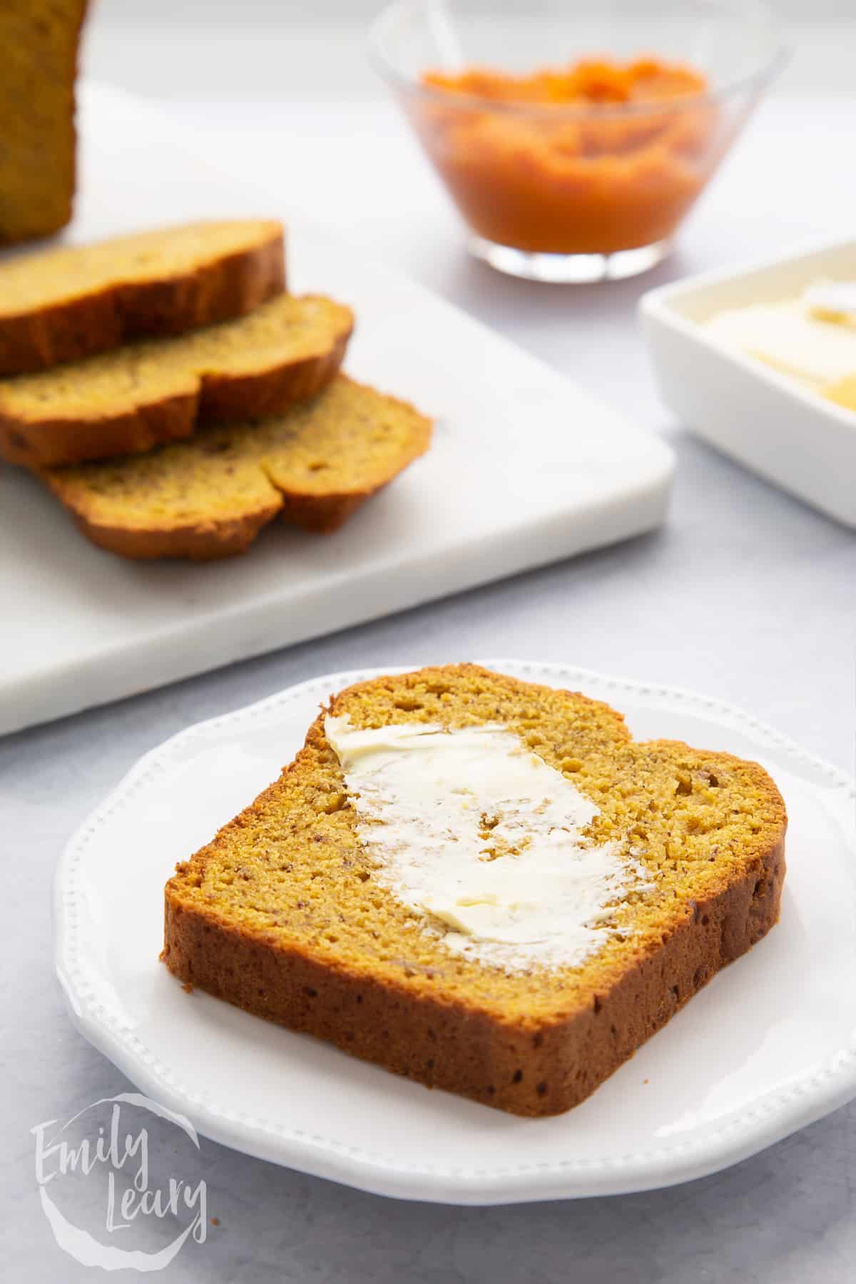 A buttered slice of pumpkin banana bread on a white plate.