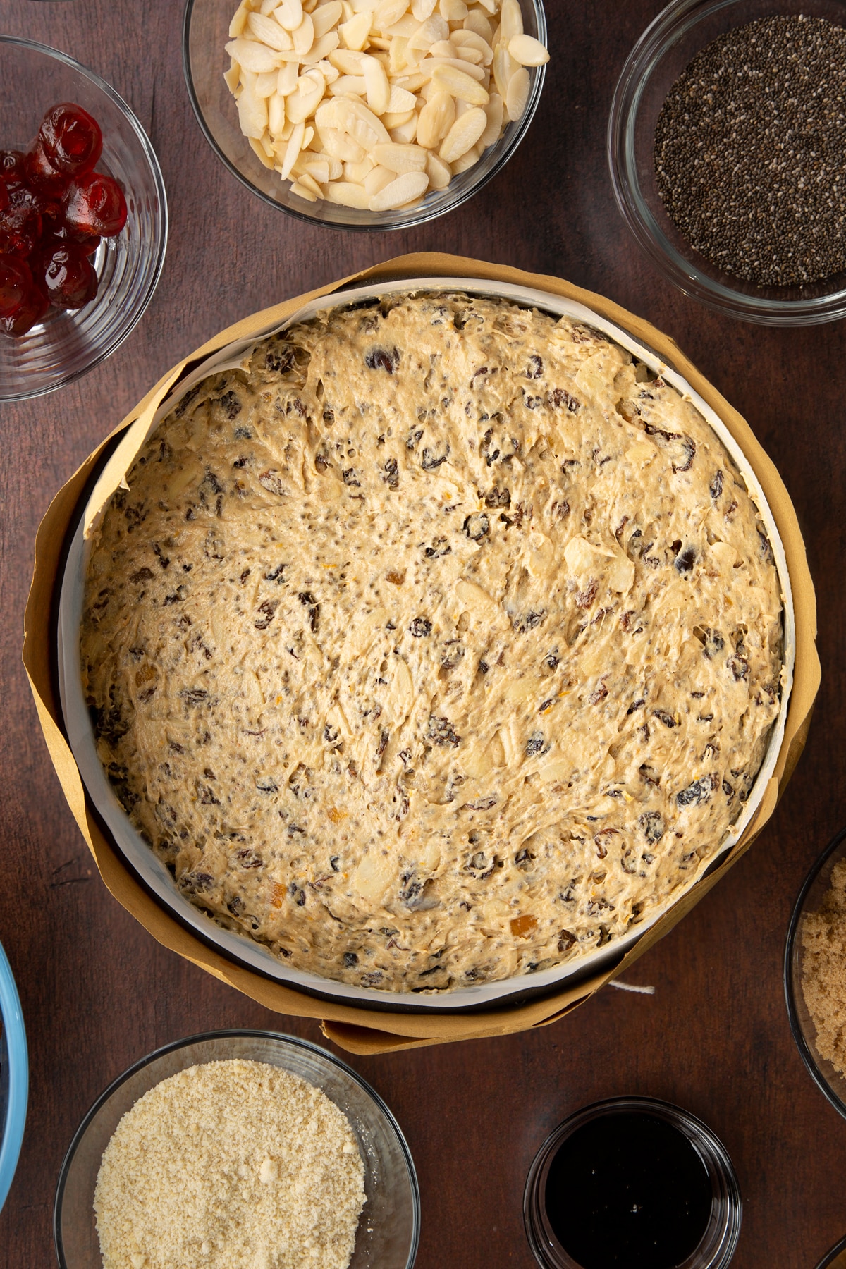 Vegan Christmas cake batter in a cake tin lined with baking paper and wrapped in brown paper, tied with string.
