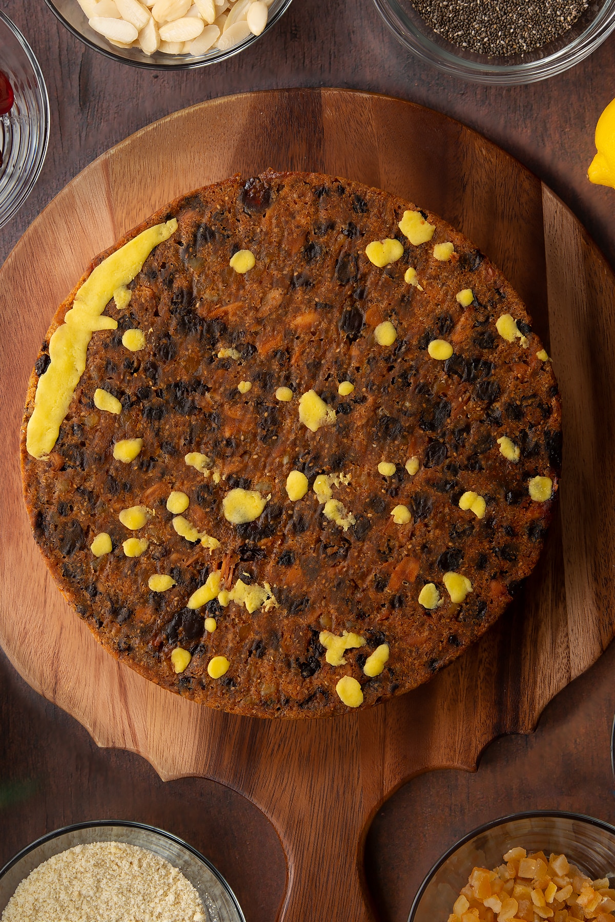 Vegan Christmas cake, upside down on a wooden board. Any dips are filled with small pieces of marzipan.