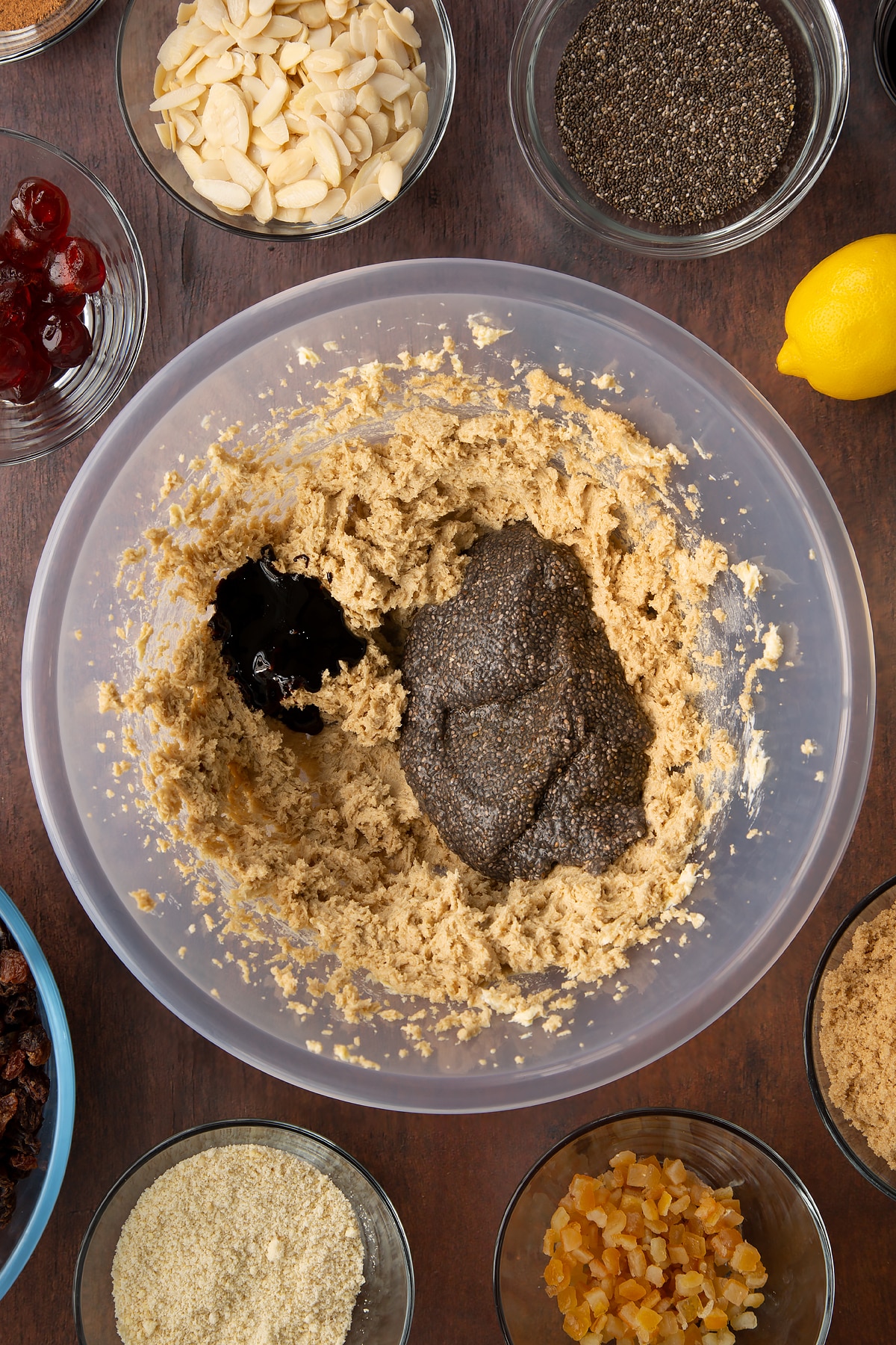 Vegan butter and brown sugar whisked together, topped with the chia "egg" and black treacle in a large plastic bowl. Ingredients to make vegan Christmas cake surround the bowl.