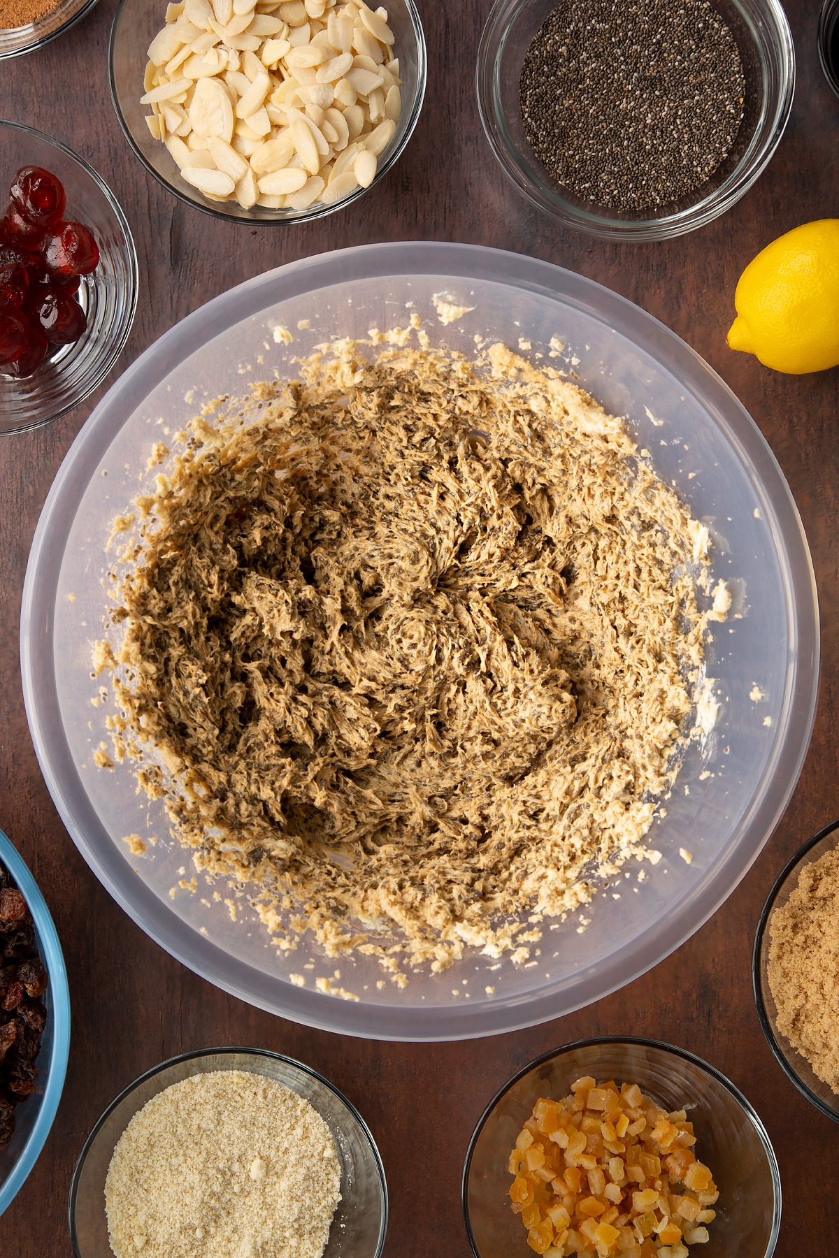 Vegan butter, brown sugar, chia "egg" and black treacle, whisked together in a large plastic bowl. Ingredients to make vegan Christmas cake surround the bowl.