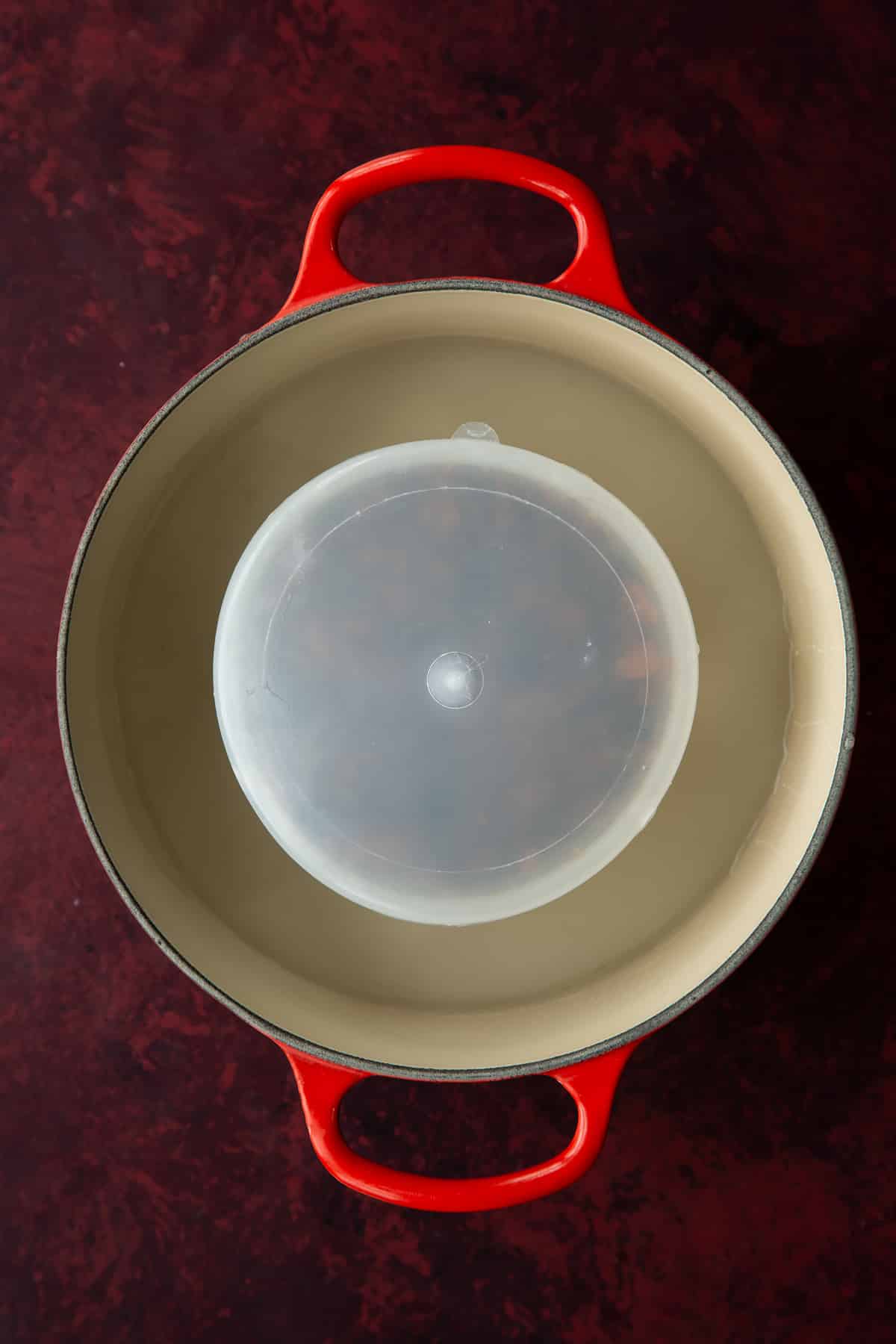 Vegan Christmas pudding batter in a pudding basin with the lid on. The basin in a pan that is part filled with water.