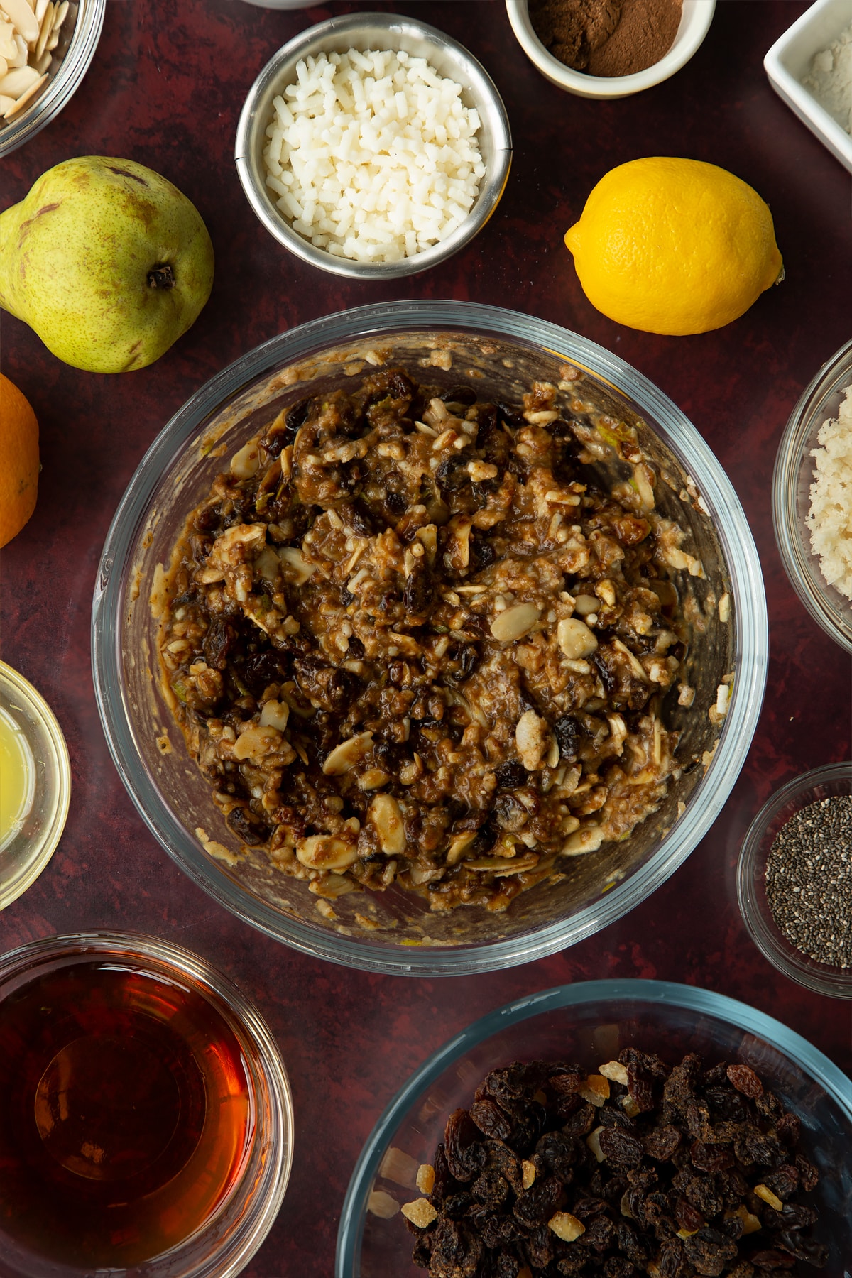 Vegan Christmas pudding batter in a glass bowl. Ingredients to make vegan Christmas pudding surround the bowl.