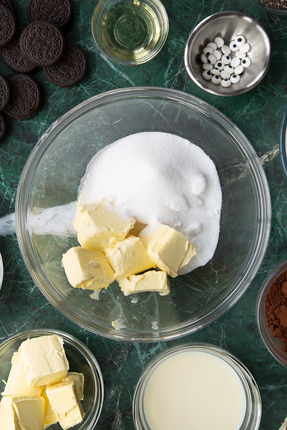 Vegan butter and caster sugar in a glass mixing bowl. Ingredients to make vegan Halloween cupcakes surround the bowl.