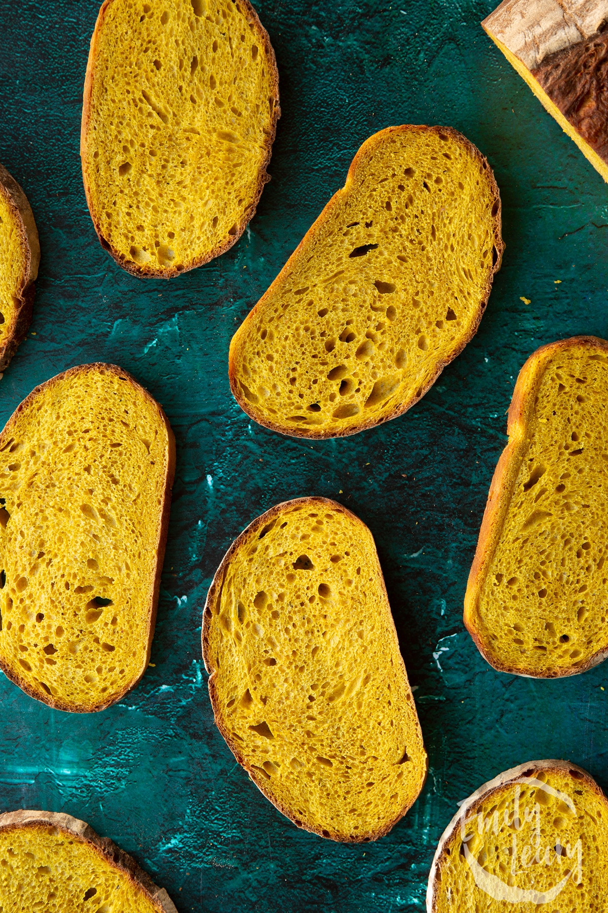 Slices of pumpkin sourdough bread arranged on a dark green surface.