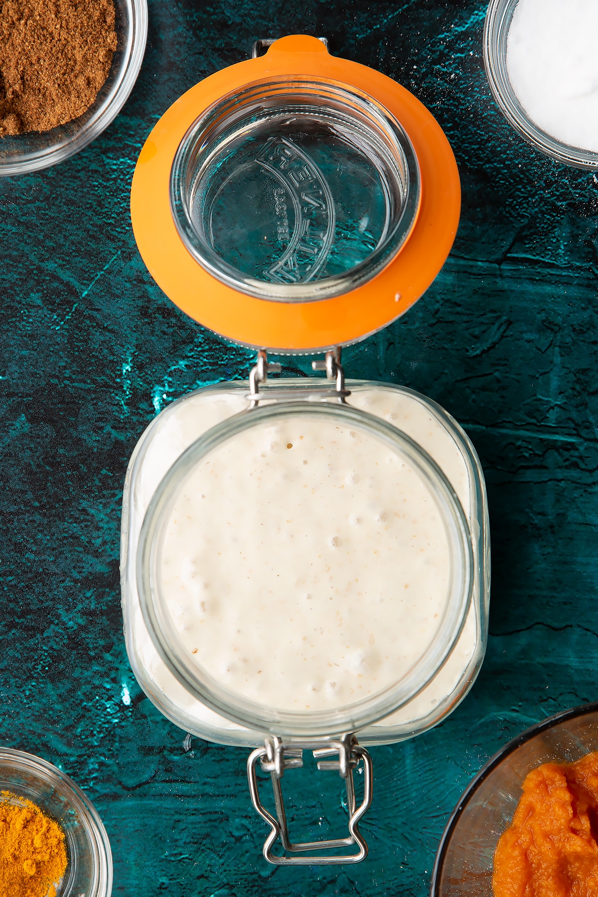 Freshly risen sourdough starter in a jar. Ingredients to make pumpkin sourdough bread surround the jar.