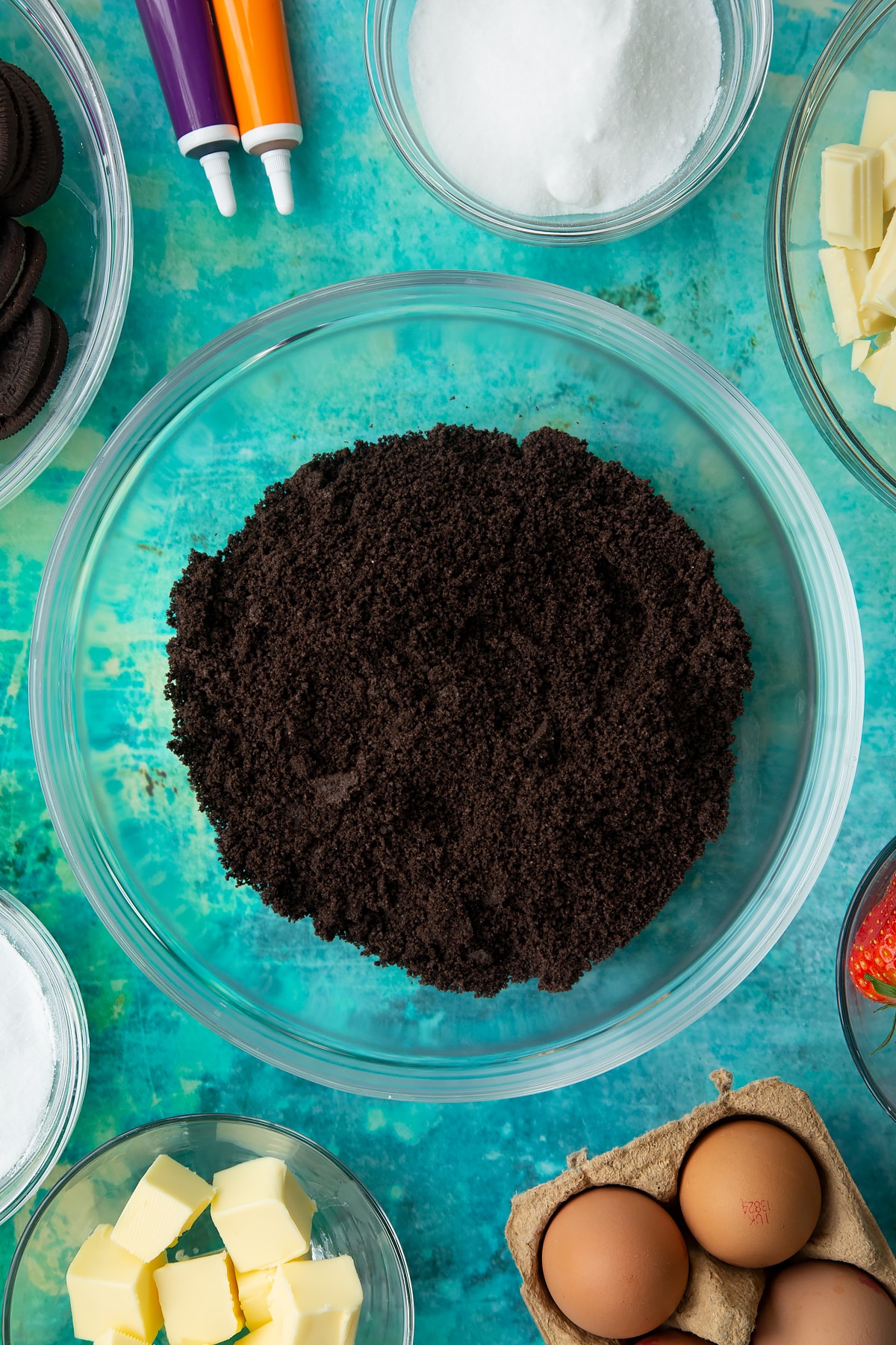 Oreo biscuit crumb in a bowl. Ingredients to make Halloween cheesecake surround the bowl.