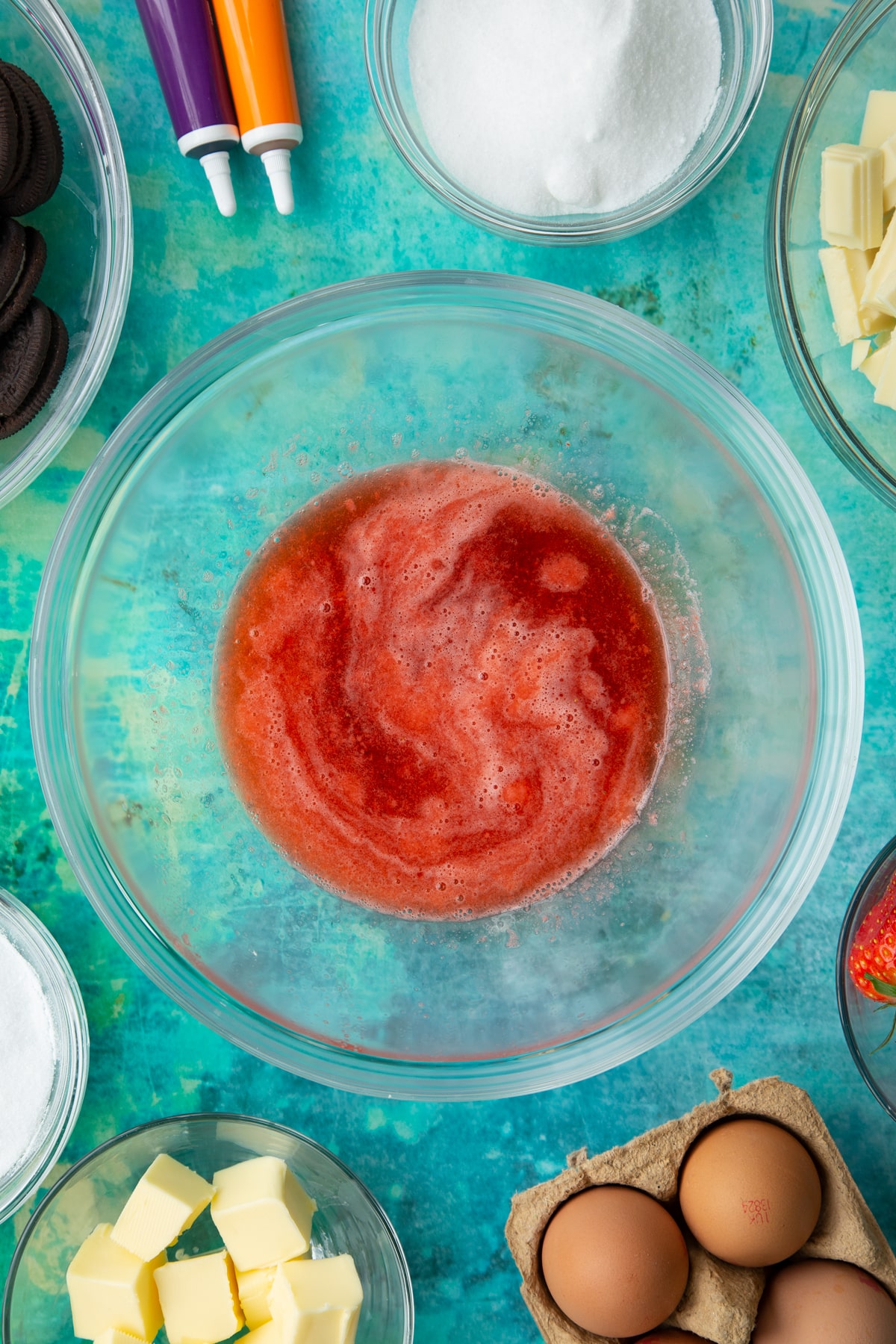 Strawberry juice in a bowl. Ingredients to make Halloween cheesecake surround the bowl.