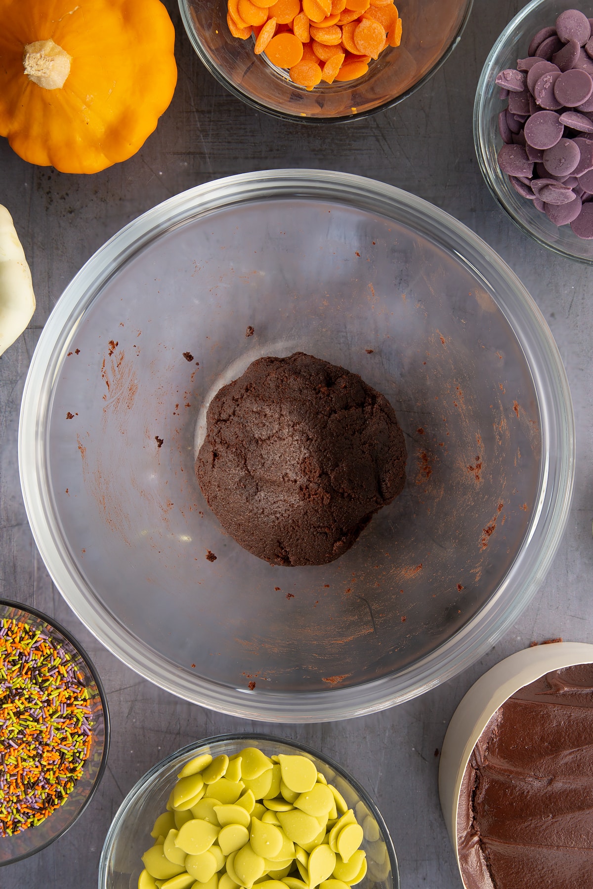 Chocolate fudge cake broken down and gathered into a ball in a bowl. Ingredients to make Halloween cake pops surround the bowl.