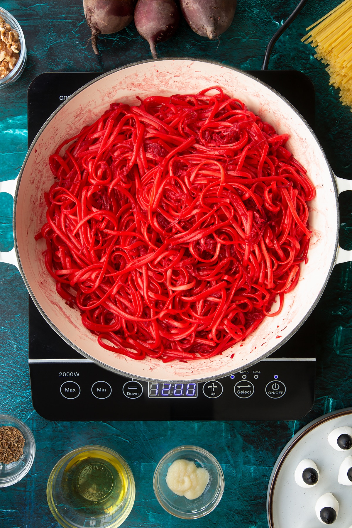 Beetroot pasta in a pan. Ingredients to make a Halloween pasta recipe surround the pan.