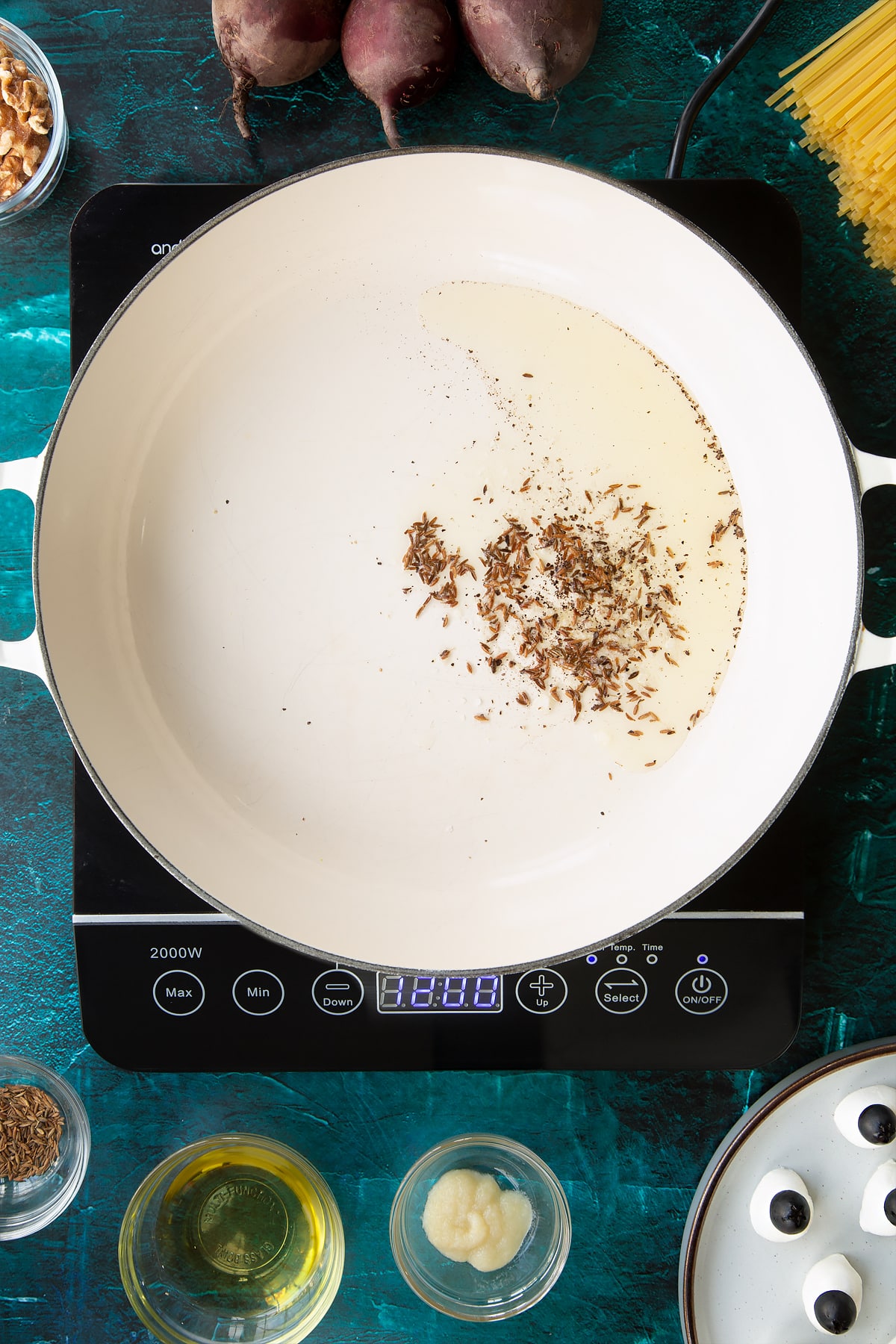 Cumin seeds in oil in a pan. Ingredients to make a Halloween pasta recipe surround the pan.