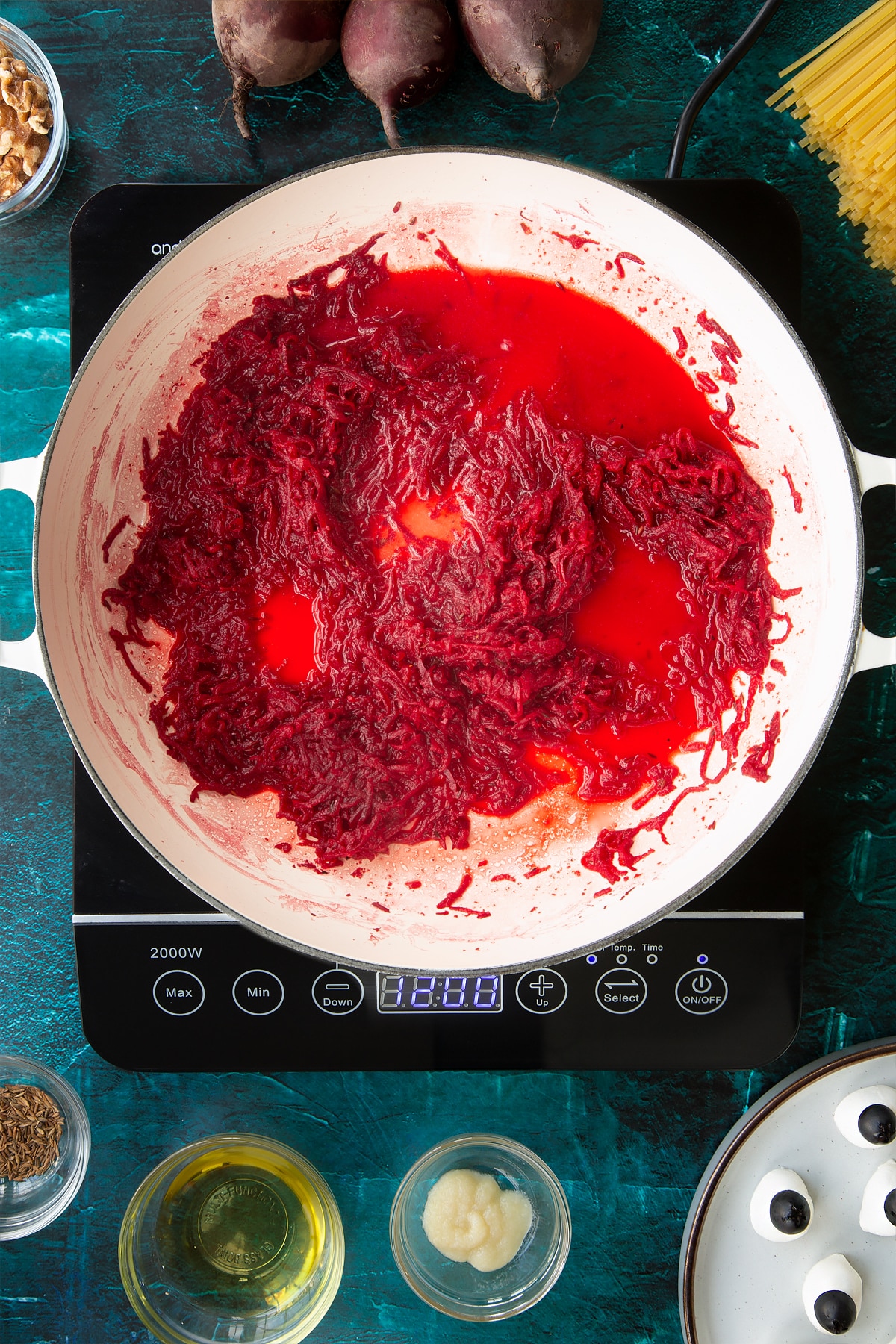 Sweated beetroot in a pan with added water. Ingredients to make a Halloween pasta recipe surround the pan.