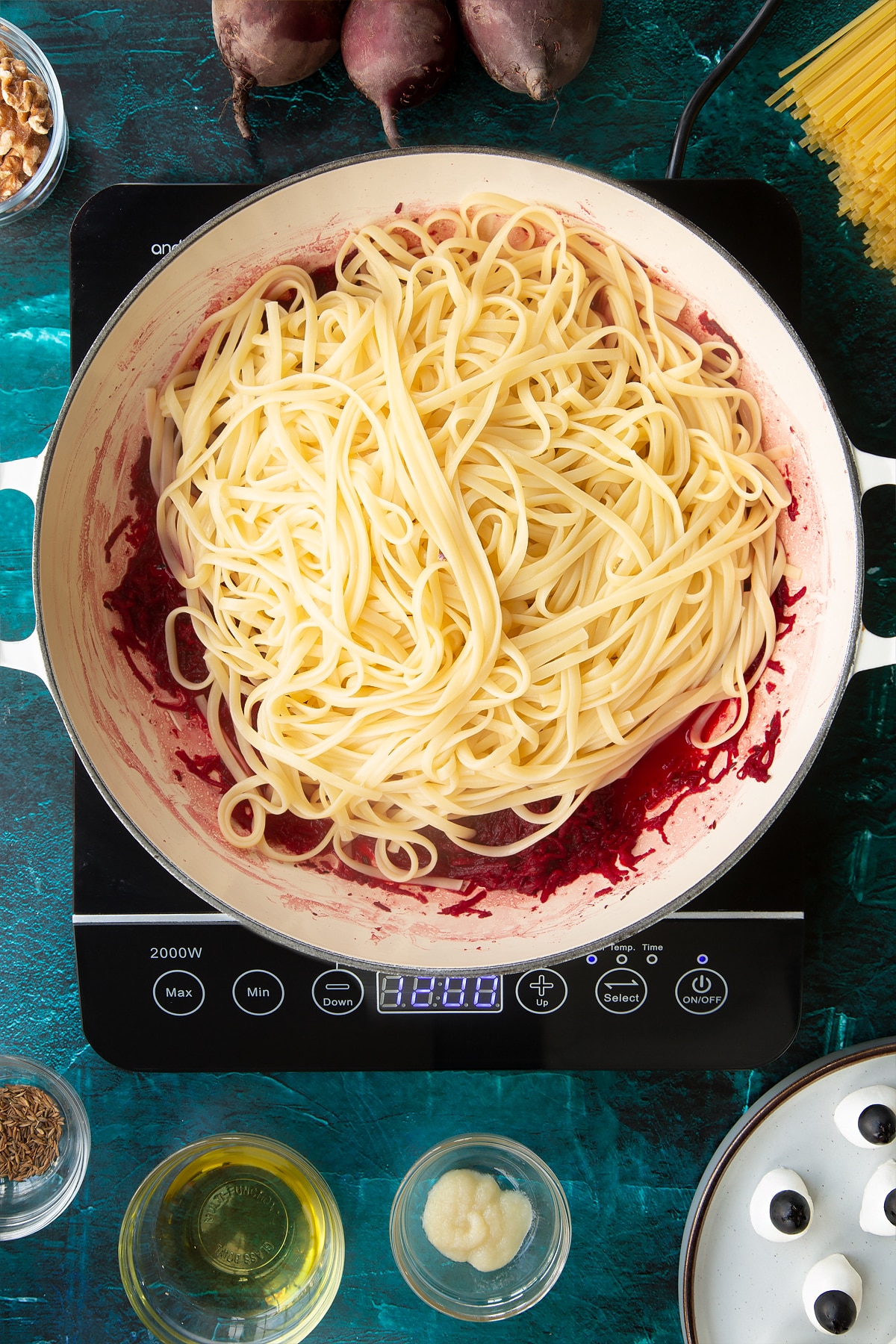 Beetroot in a pan with linguine on top. Ingredients to make a Halloween pasta recipe surround the pan.