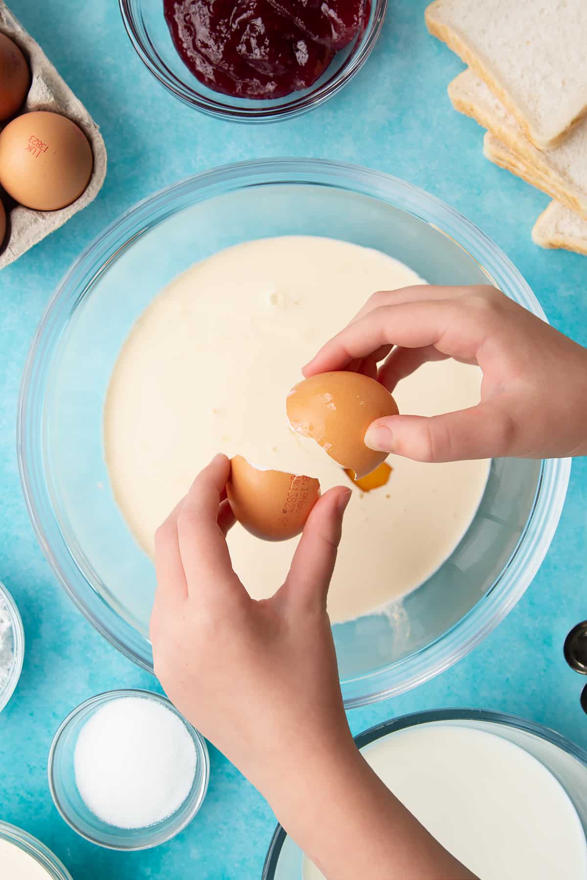 Overhead shot of cracking eggs into a clear bowl.