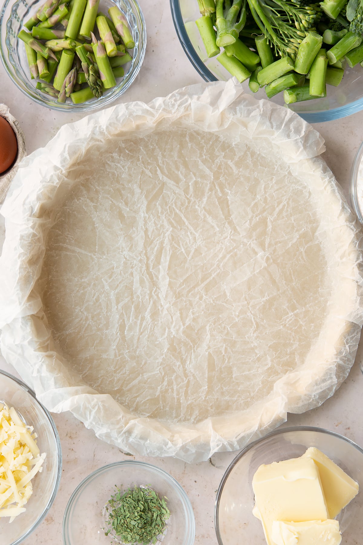 Overhead shot of some baking paper laid over the top of the pastry in a pie tin.