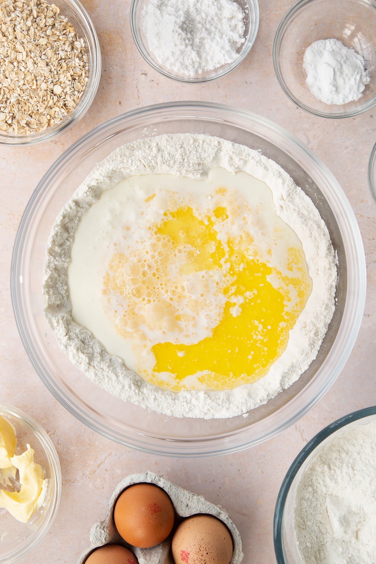 Flour, salt, bicarbonate of soda and icing sugar in a bowl. Beaten eggs, milk and melted butter are in a well in the middle. Ingredients to make gluten free crepes surround the bowl.