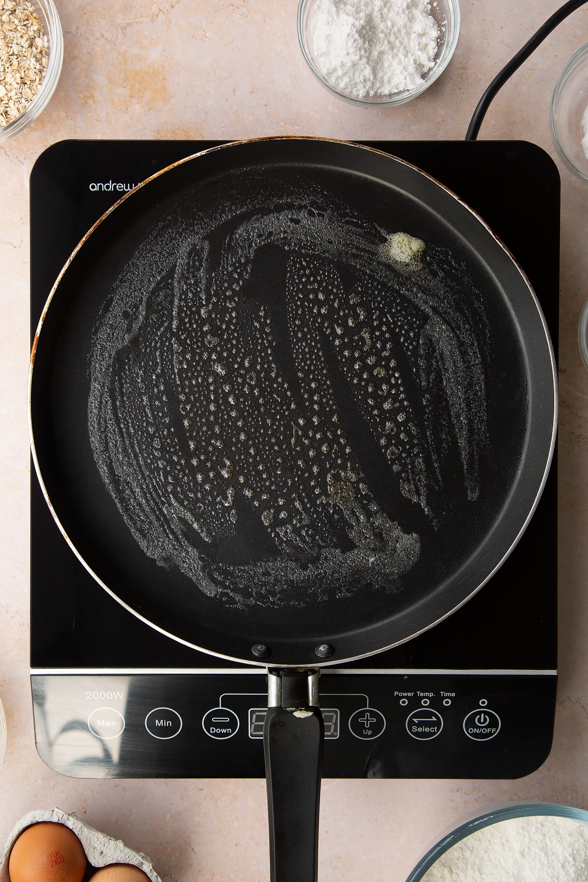 Butter melted in a crepe pan. Ingredients to make gluten free crepes surround the bowl.