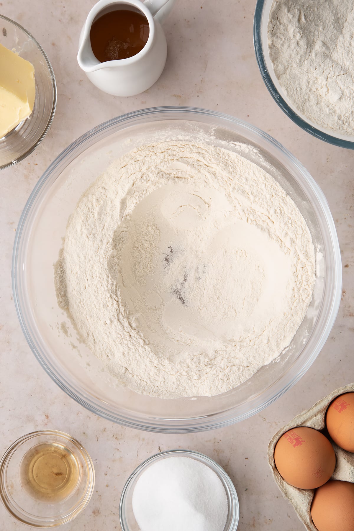 flour and sugar in a large clear bowl with a well in the middle.