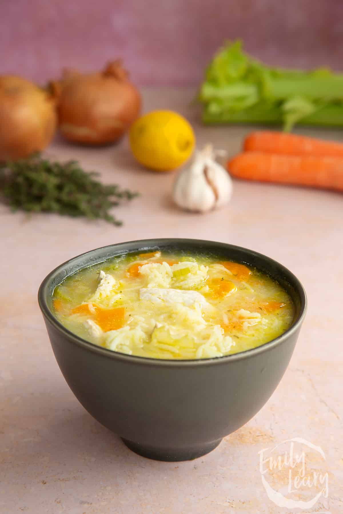 Bowl of finished turkey rice soup served in a black bowl with some of the ingredients for the recipe in the background.