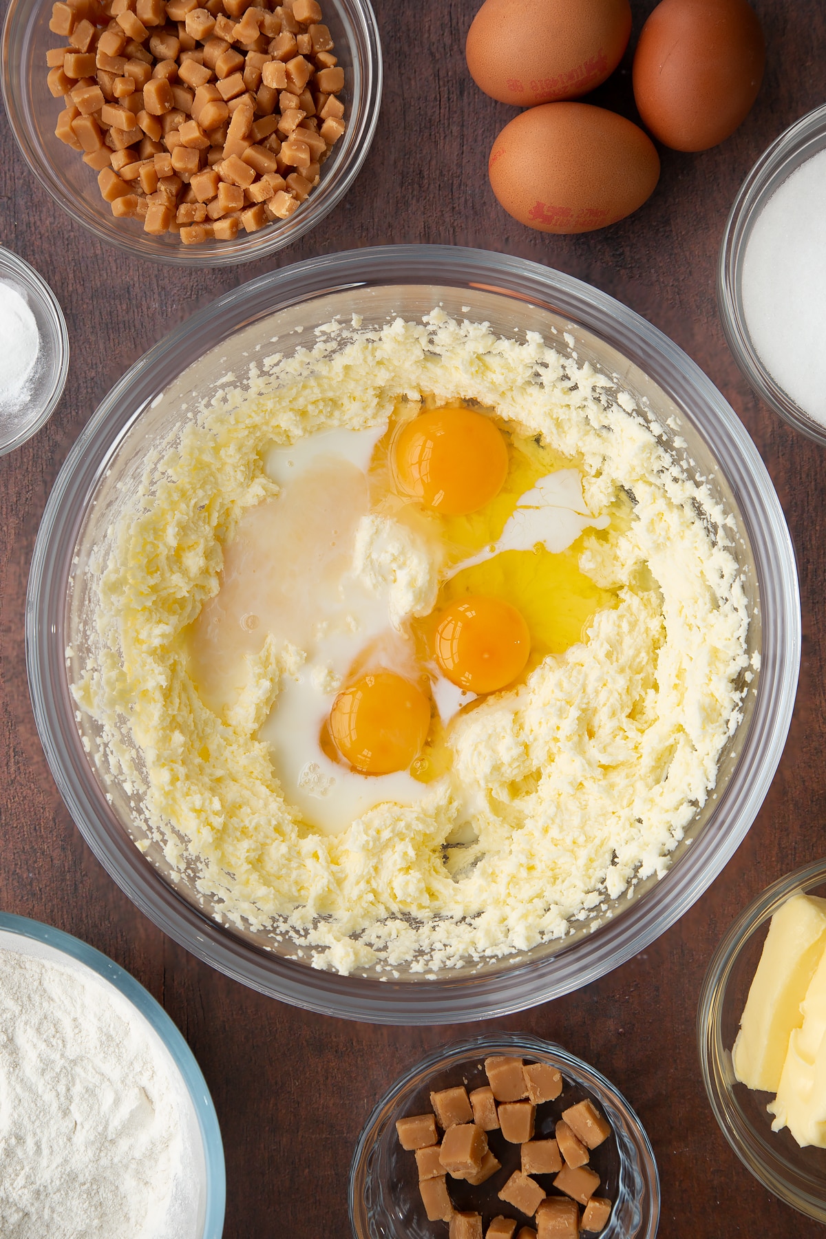 whisked butter and sugar mixture topped with milk, eggs and vanilla in a large clear bowl.