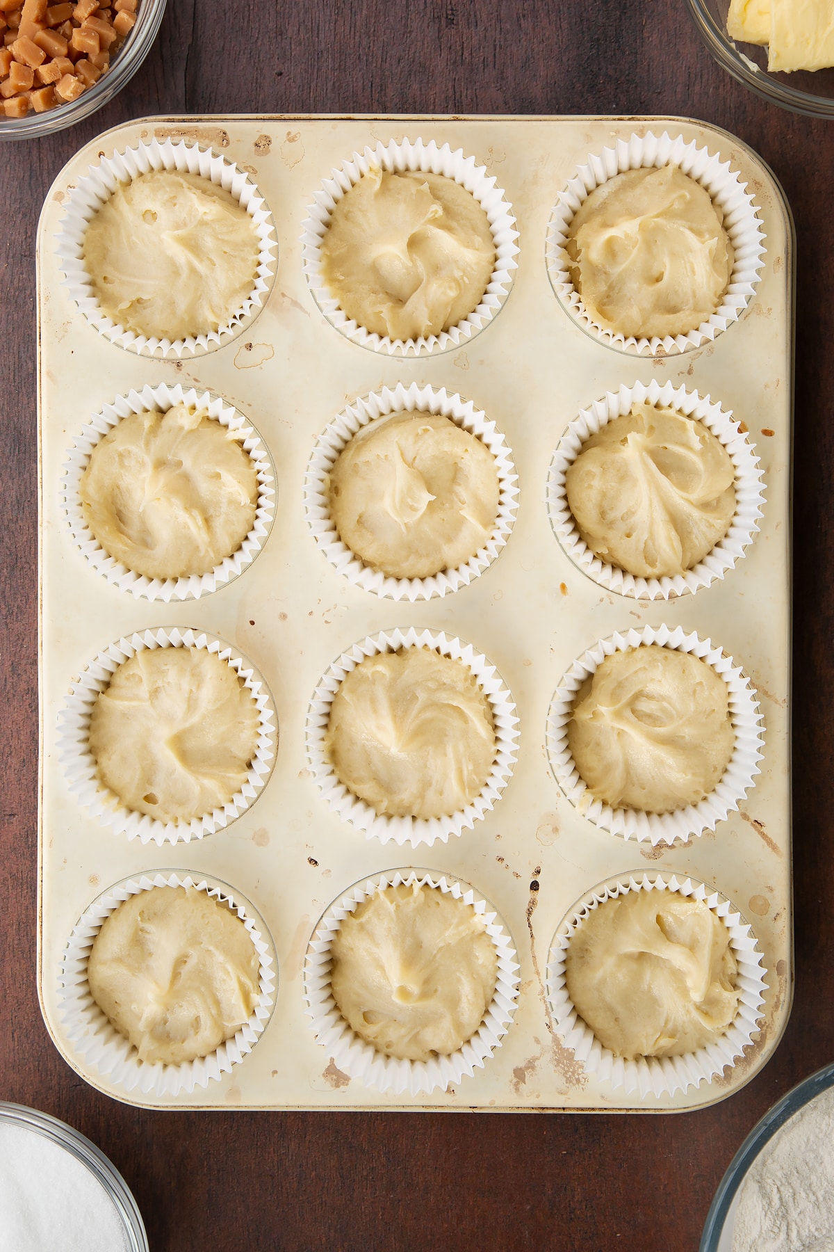 12 bun cases in a metal bun tray filled with vanilla cake batter.