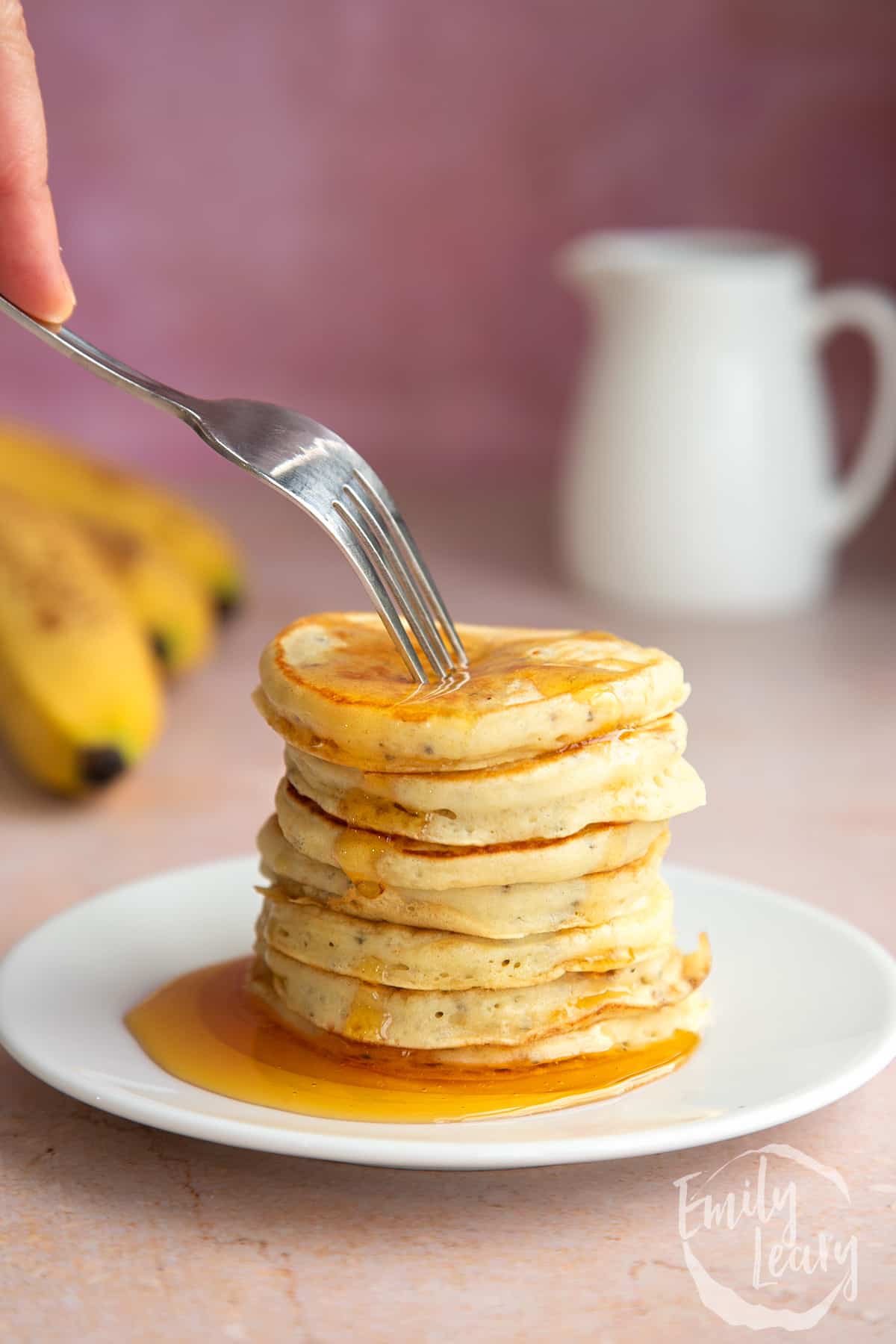 A stack of vegan chia pancakes on a small white plate, drizzled with golden syrup. A fork digs in.
