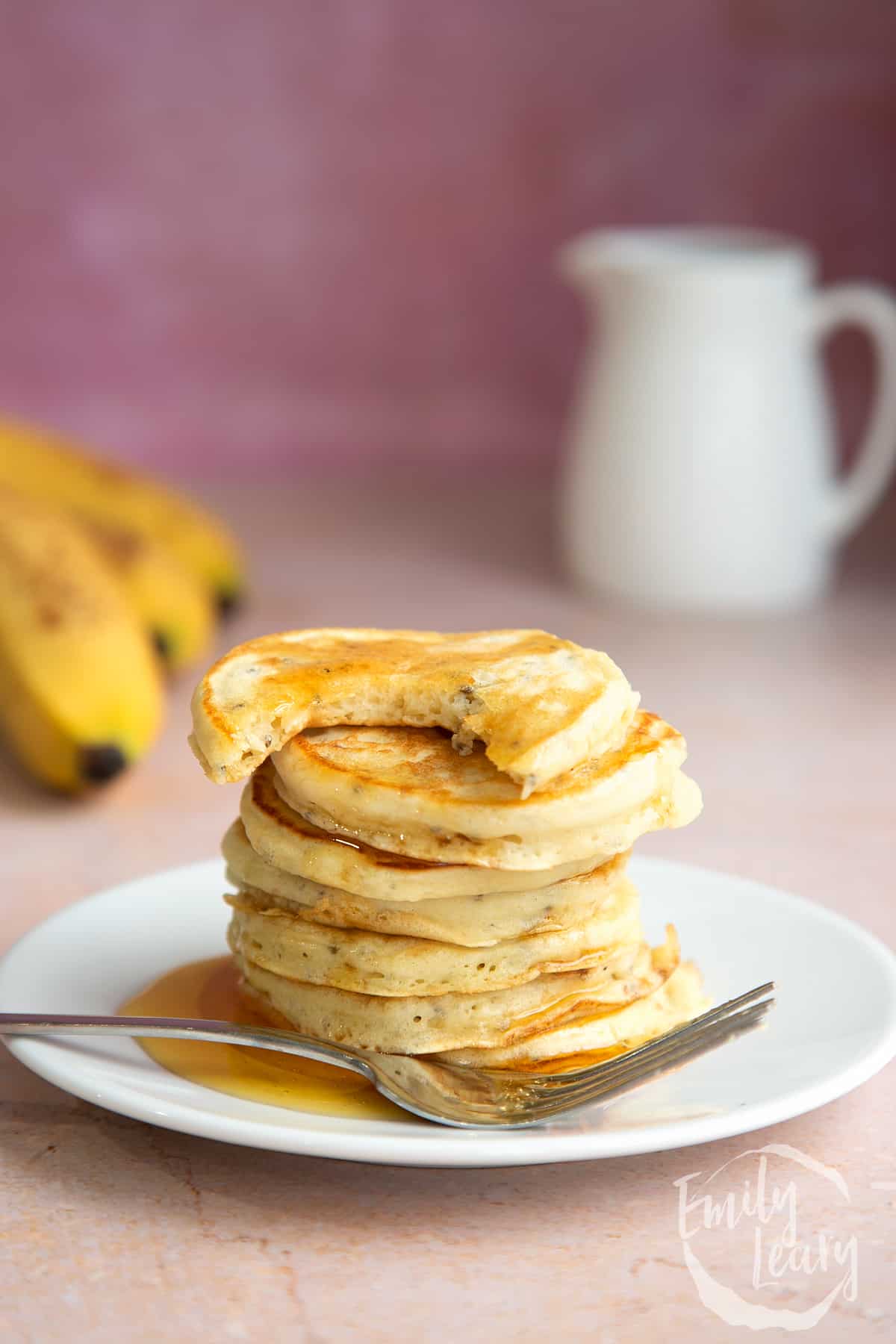 A stack of vegan chia pancakes on a small white plate, drizzled with golden syrup. The top one is bitten. A fork rests on the plate.