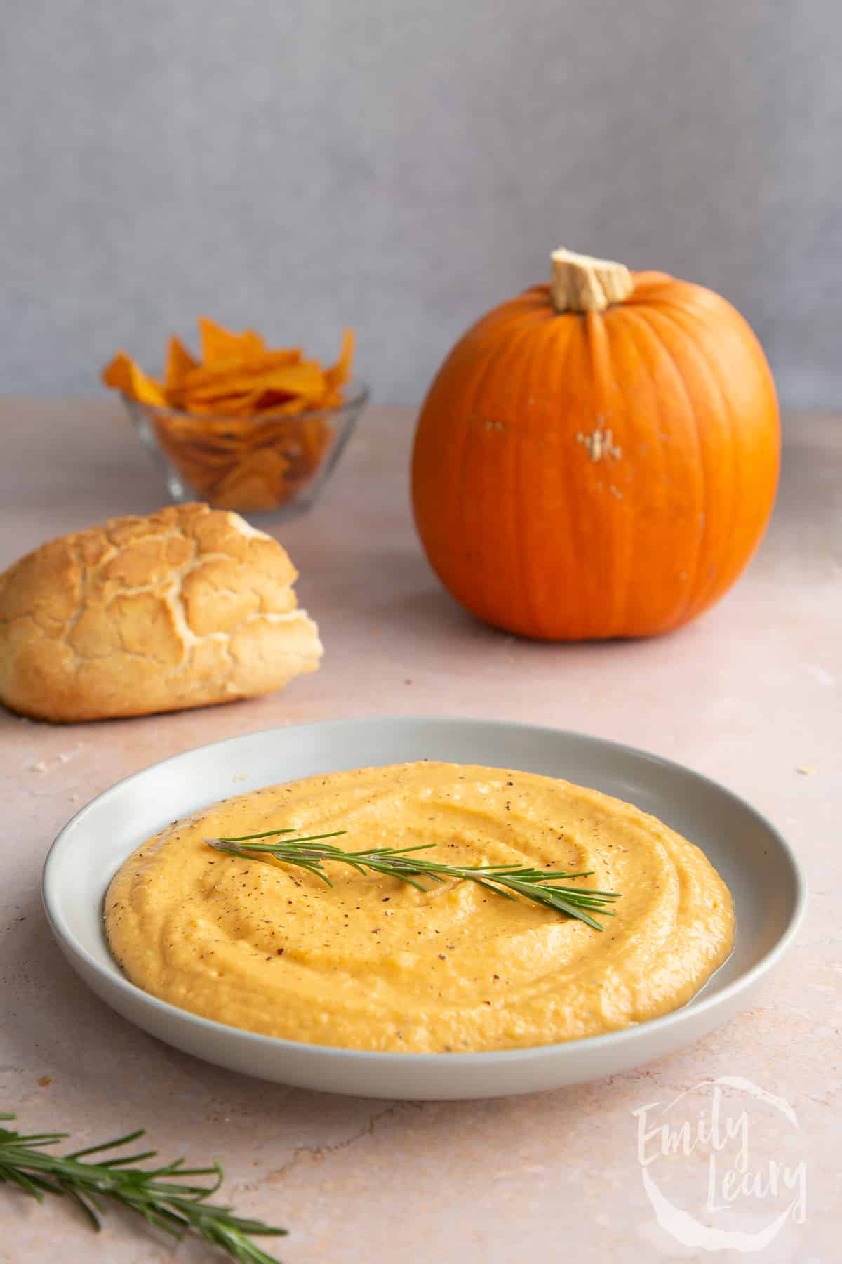 Vegan pumpkin dip in a shallow grey bowl with a sprig of rosemary.