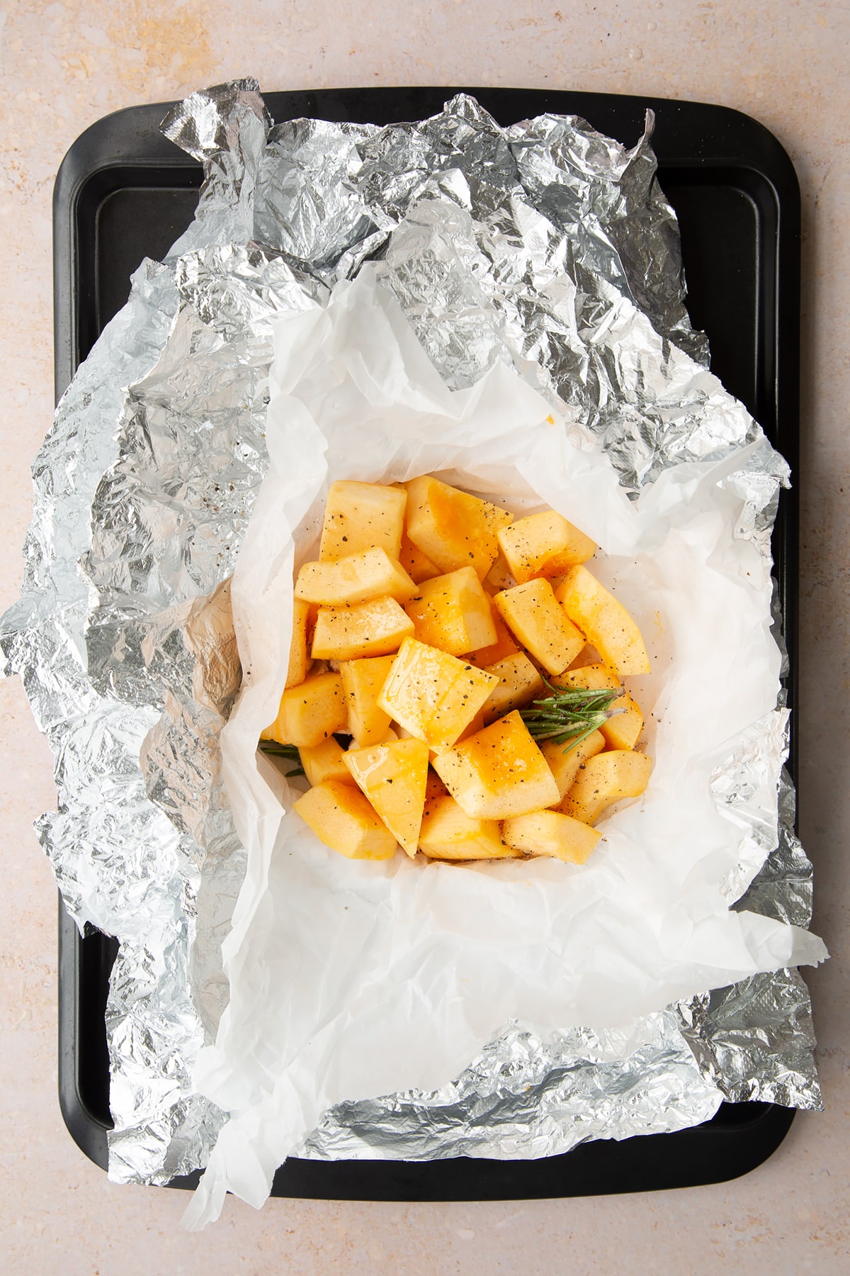 Chopped pumpkin, garlic and rosemary in a half open paper and foil packet on a baking tray.