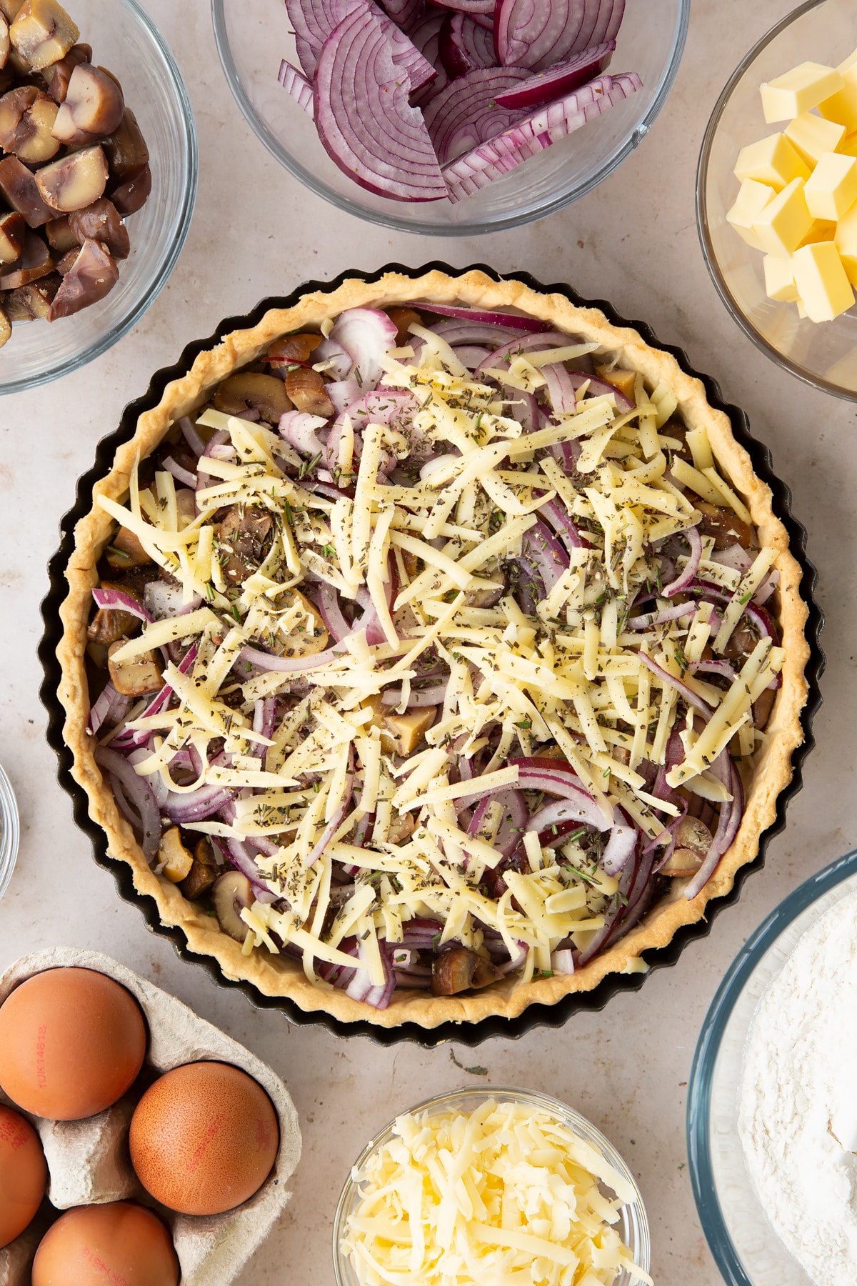 Overhead shot of the red onion and chestnut pieces put inside the half baked pastry crust inside a pie tin.