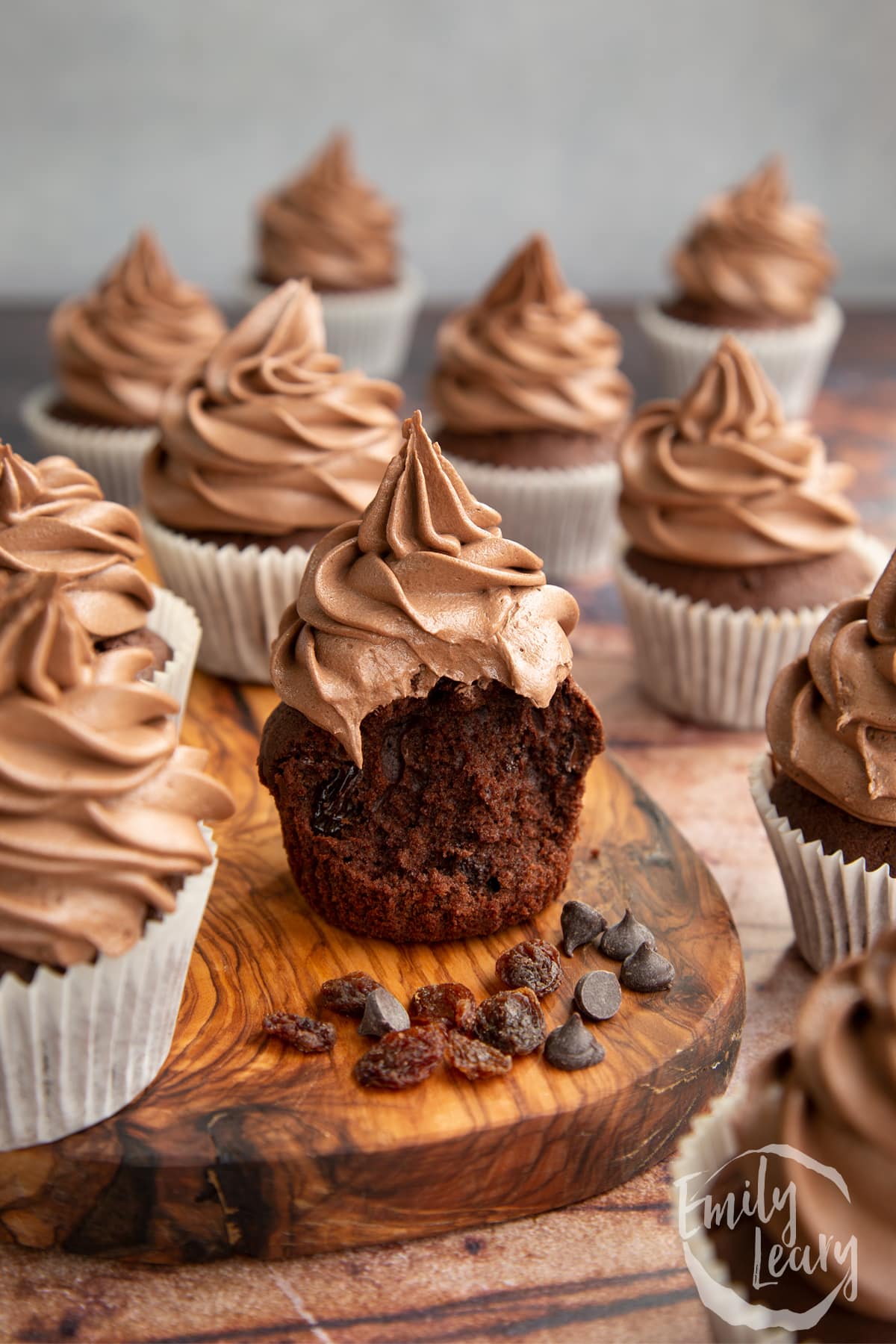 Chocolate raisin muffins with Nutella frosting on a wooden board. The muffin in the fore is unwrapped with a bite out of it.