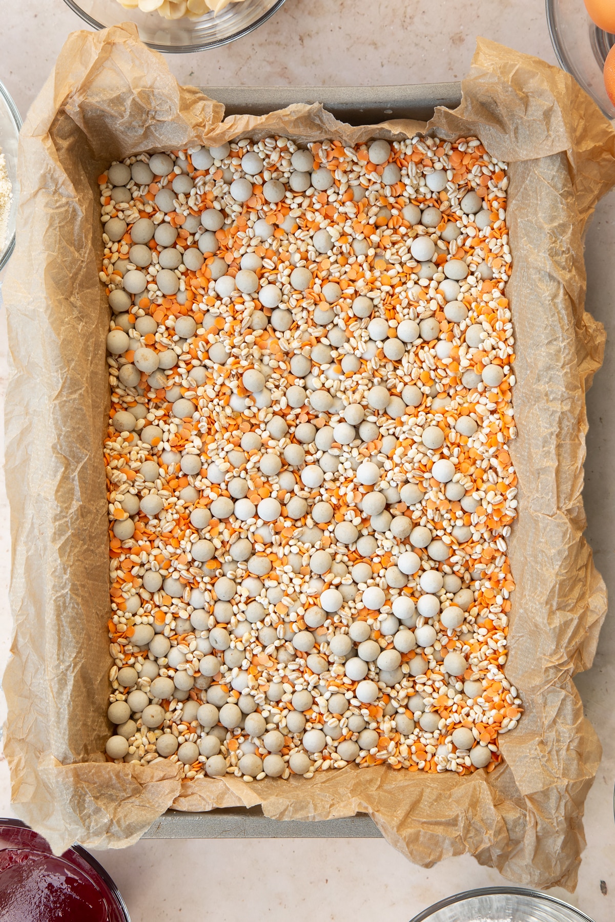 Raw pastry lining the base of a rectangular tin, lined with brown baking paper and filled with baking beans.