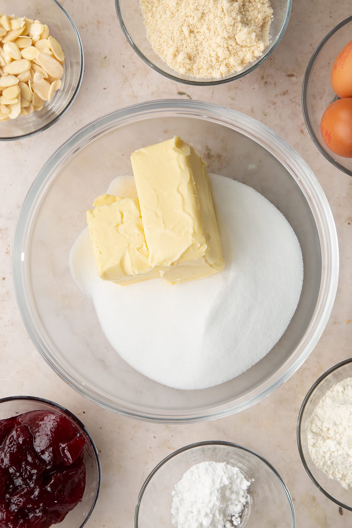 Butter and sugar in a bowl. Ingredients to make a Bakewell tray bake surround the bowl.